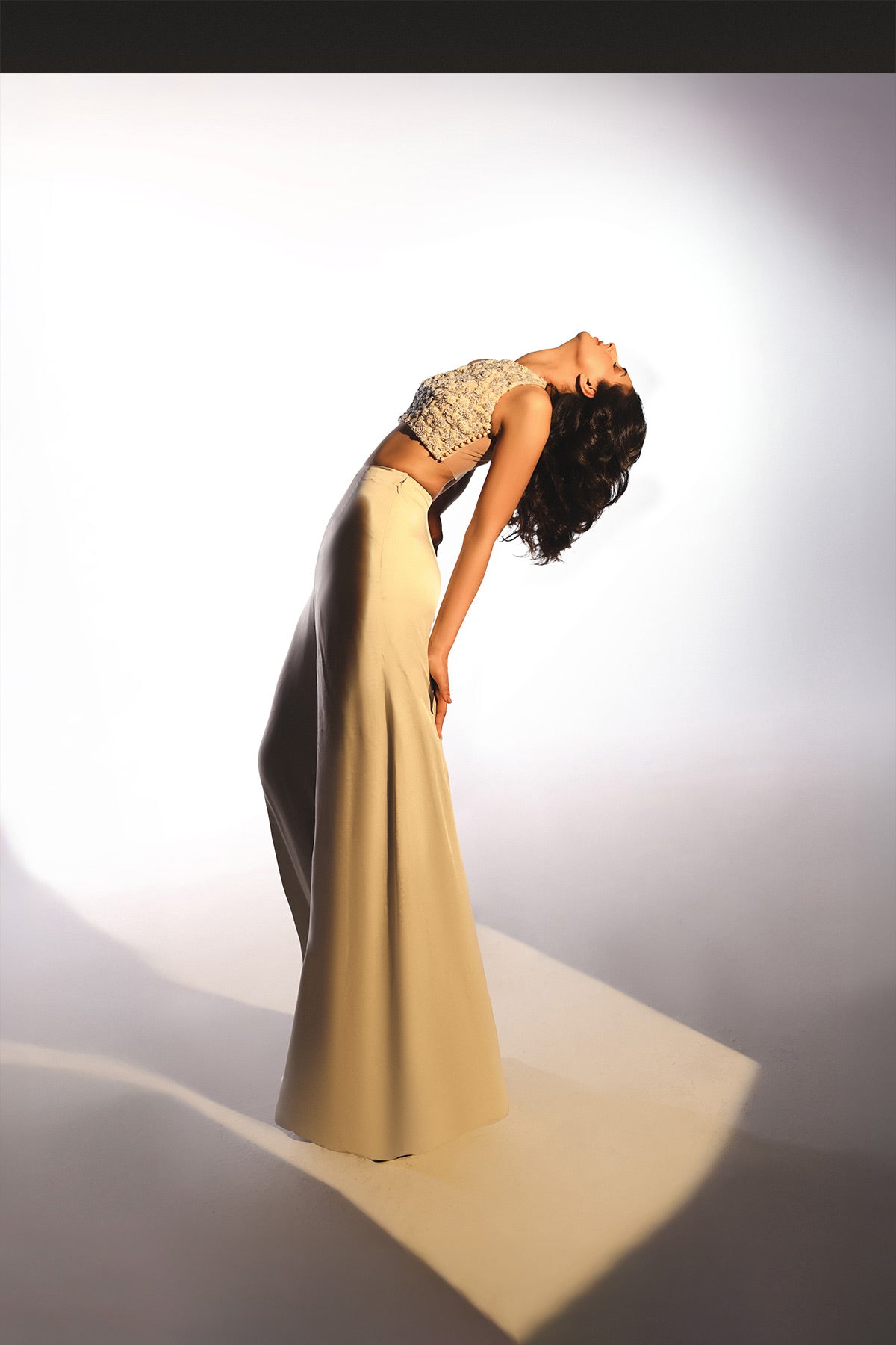 Woman in a long beige skirt and lace top posing against a white background
