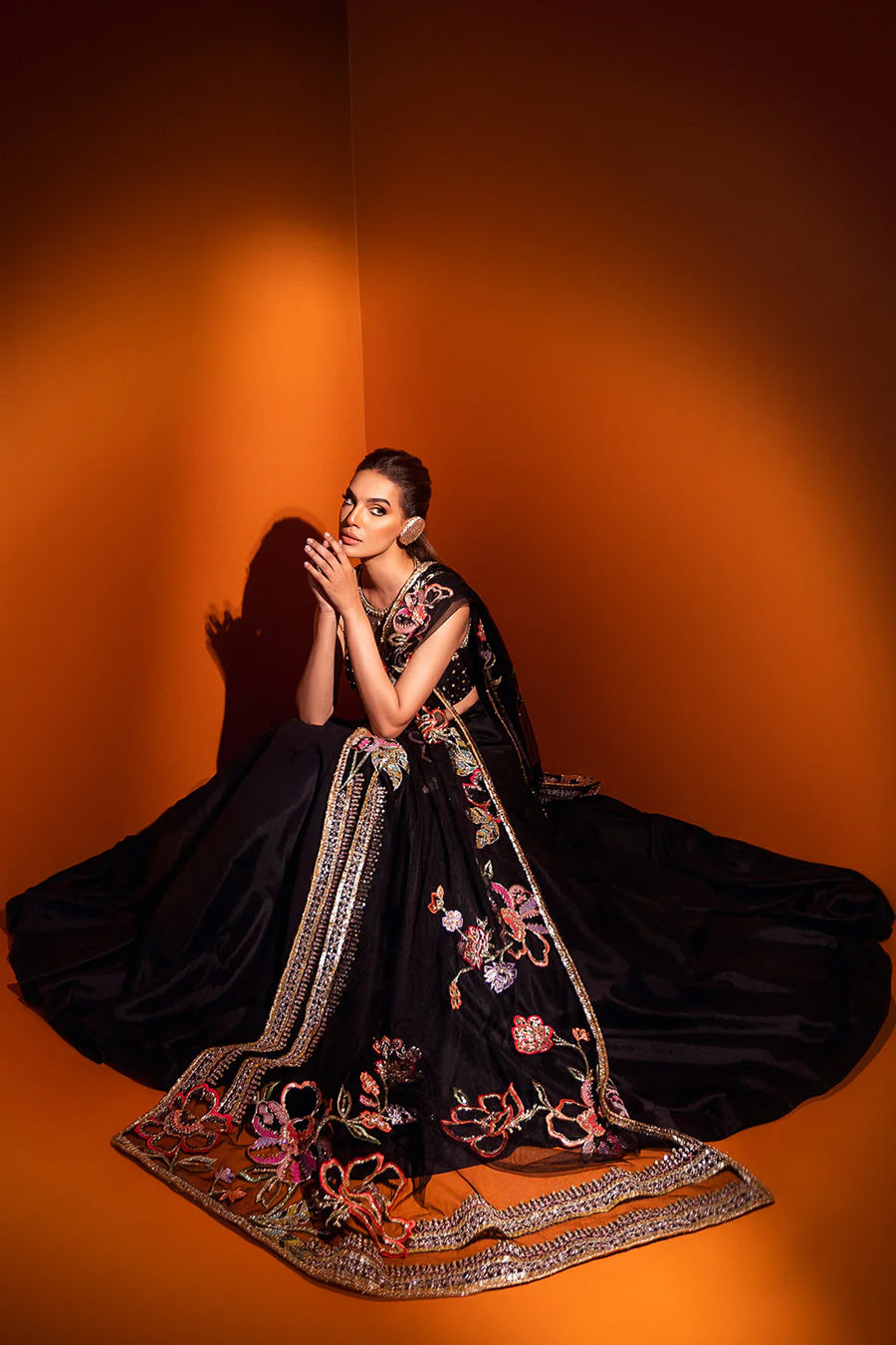 model in a seated shot wearing formal black net dupatta paired with net blouse and a silk lehenga
