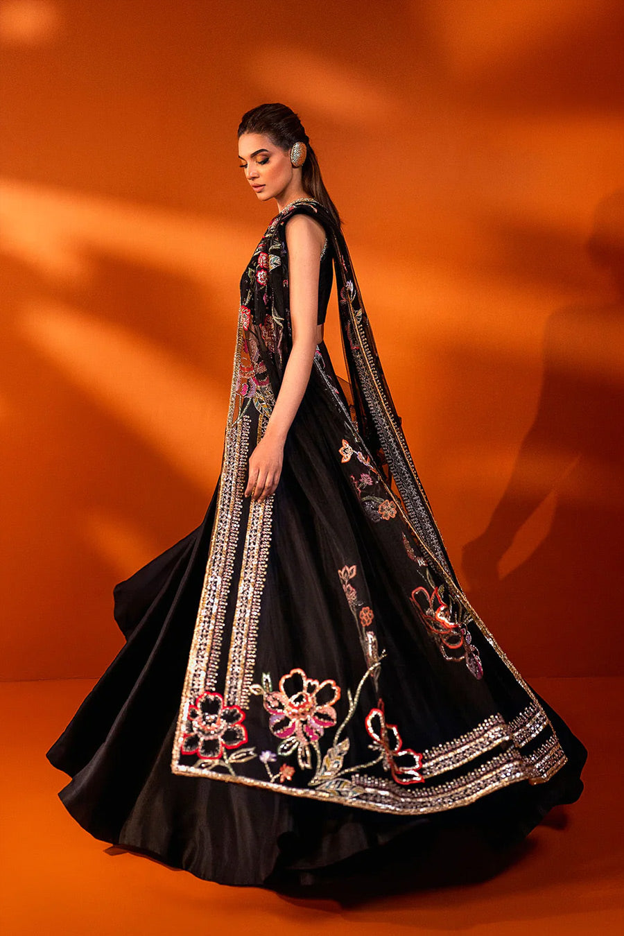 model in a side shot wearing formal black net dupatta paired with net blouse and a silk lehenga