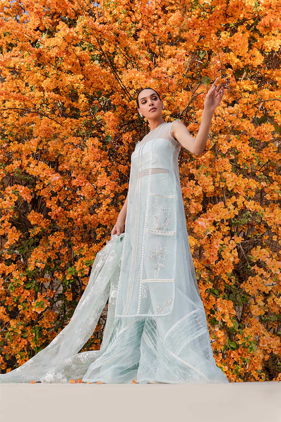 model in a low angle shot wearing a formal blue organza shirt paired with bamber silk trousers and organza dupatta