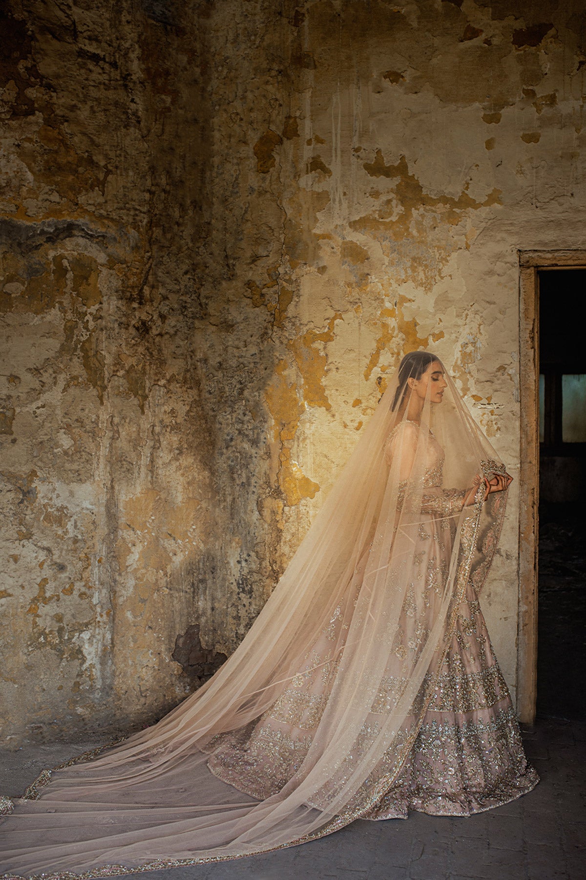 Model in a front shot wearing blush pink silk organza lehenga choli accompanied by a net dupatta and net veil