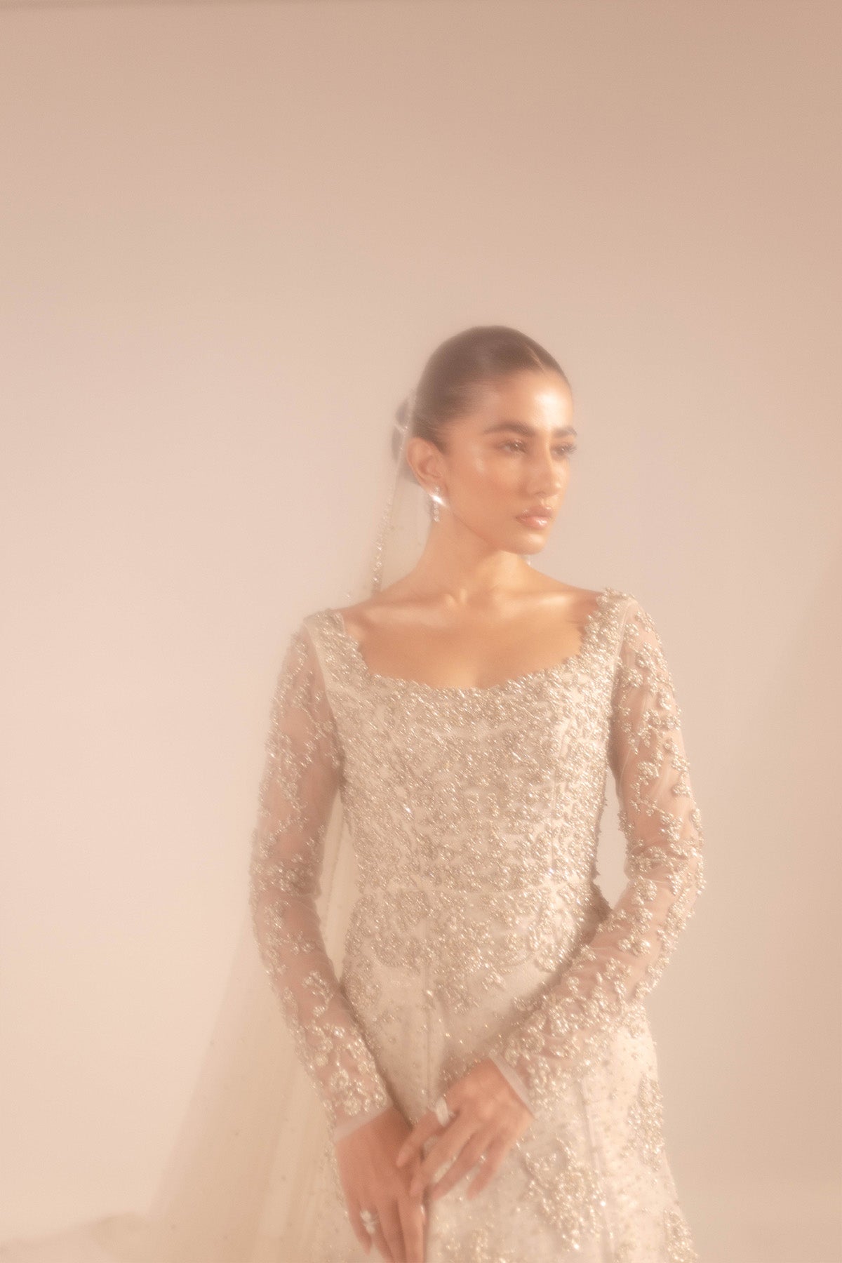 Model in a mid shot wearing a net bridal gown heavily embellished with zardozi, sequins, and crystal work