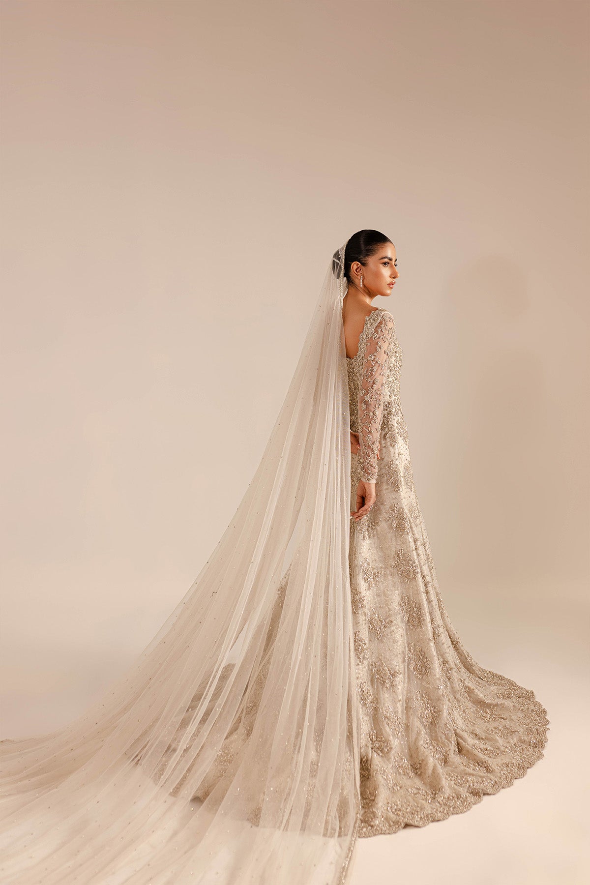 Model in a side shot wearing a net bridal gown with a mermaid fit and train and a cathedral-style veil
