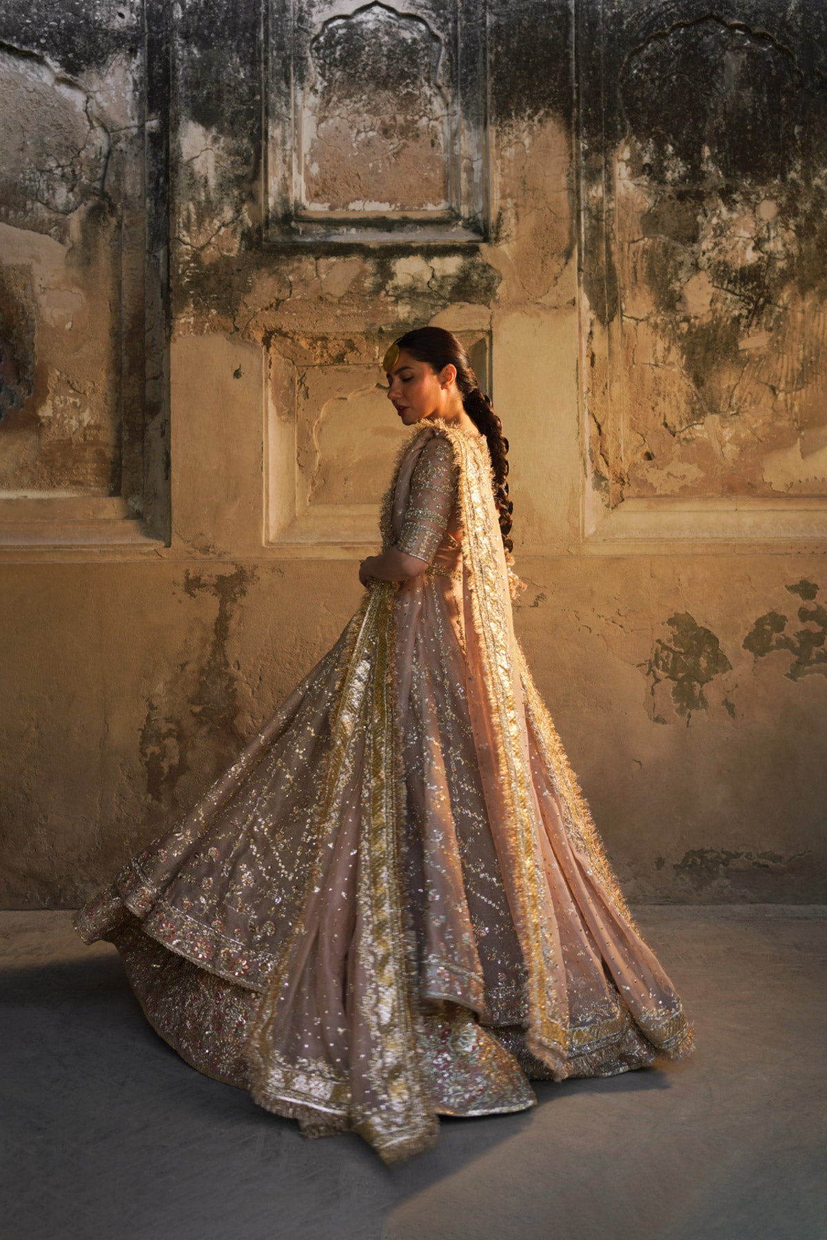 Mahira Khan in a side view angle wearing a dusty pink bridal peshwas by Zuria Dor paired with a handcrafted dupatta and an embellished lehenga