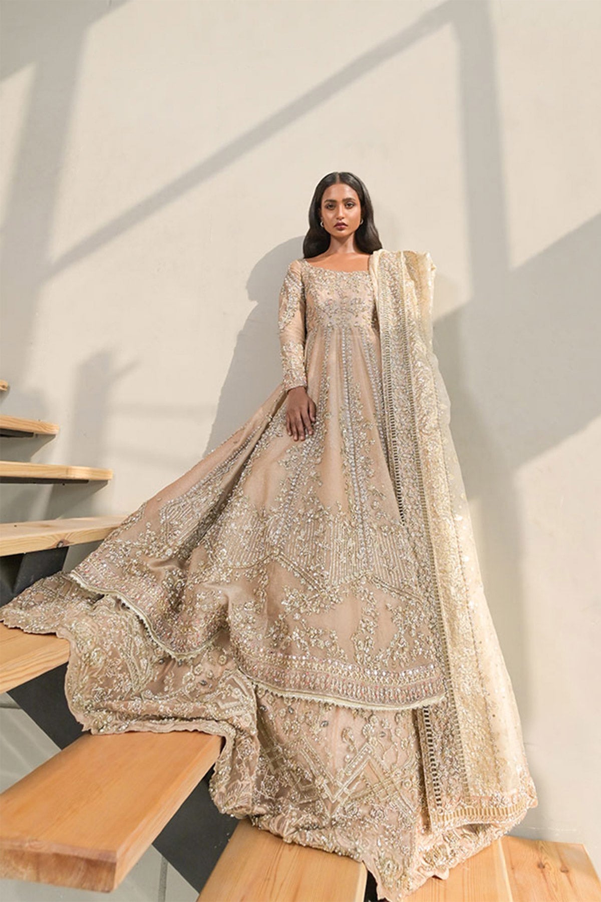 Model in a front shot wearing a dusty pink pishwas paired with lehenga along with an organza zari dupatta with colored and embellished borders