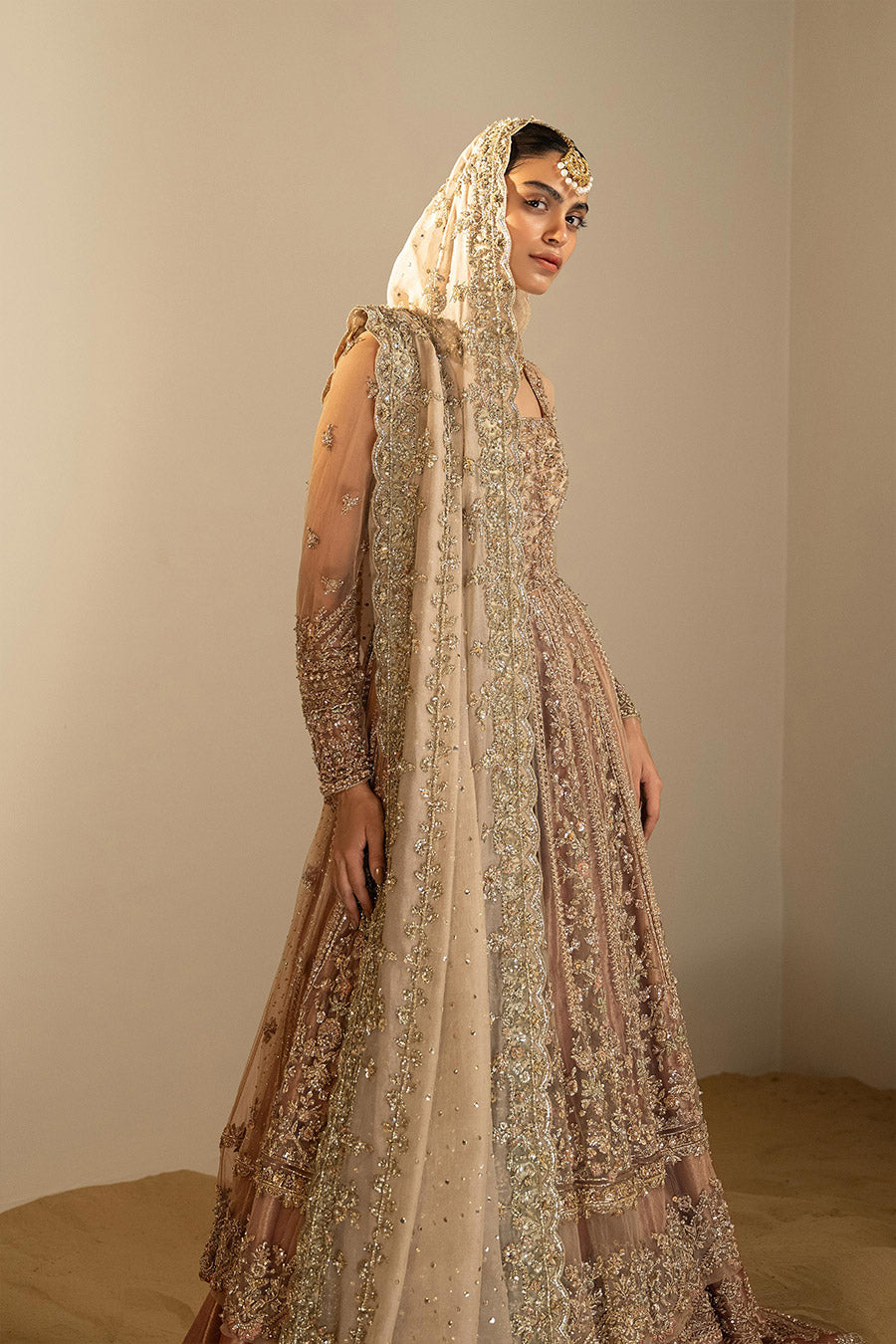 Model in a side shot wearing dusty pink net pishwas combined with a farshi sharara and a dusty pink silk organza dupatta