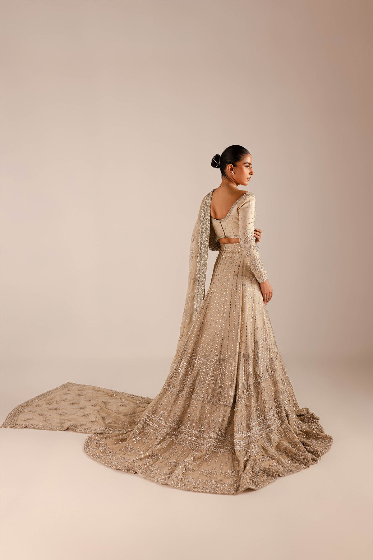 Model in a back shot wearing a gold and silver lehnga with a train and an attached drape