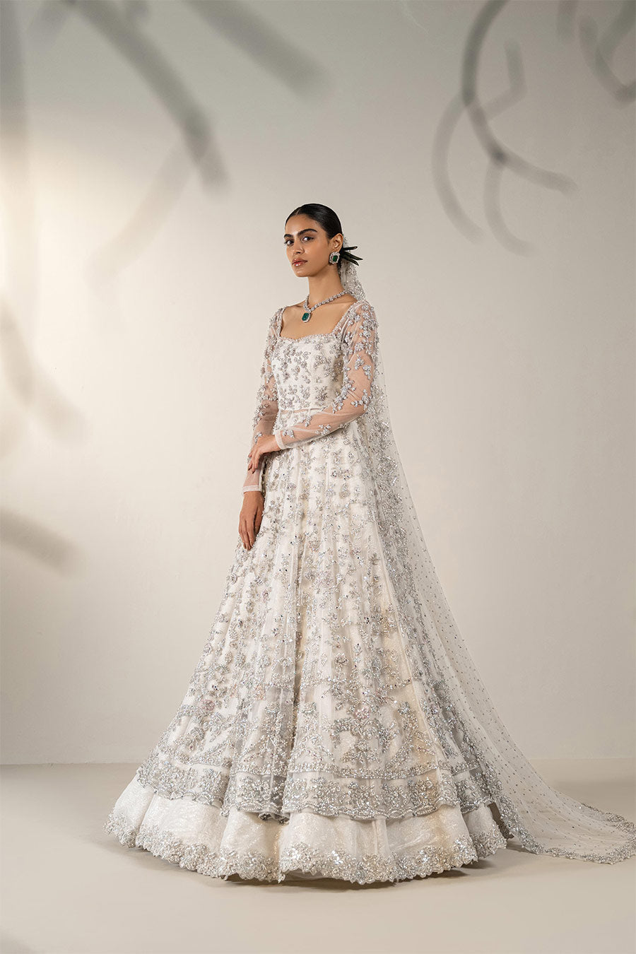 Model in a front side view shot wearing ivory bridal net pishwas paired with organza lehenga and a net veil