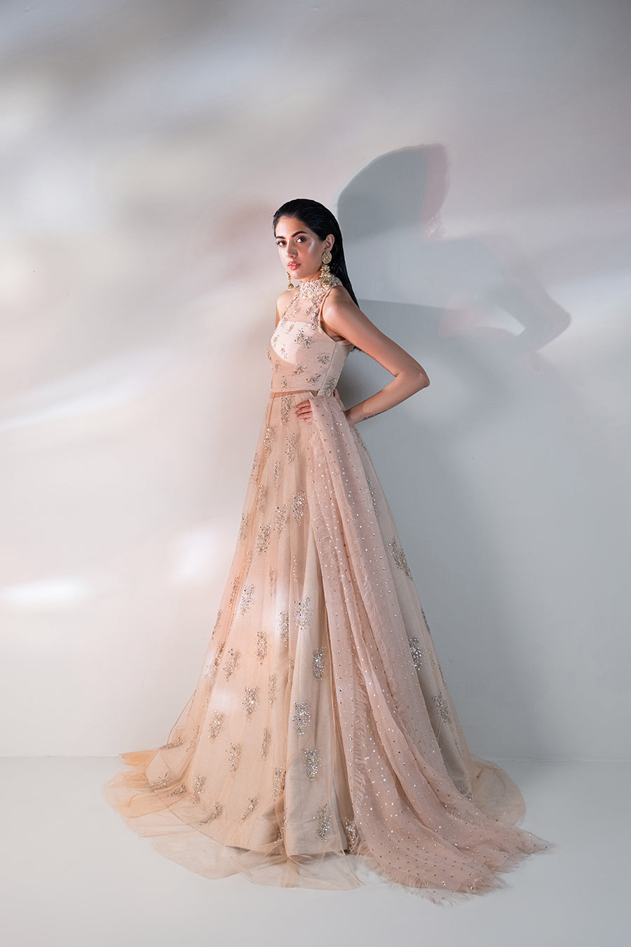 model in a side shot wearing a formal net mandarian collar with a front open slit shirt and paired with a shimmer light peach lehnga and a mokaish dupatta