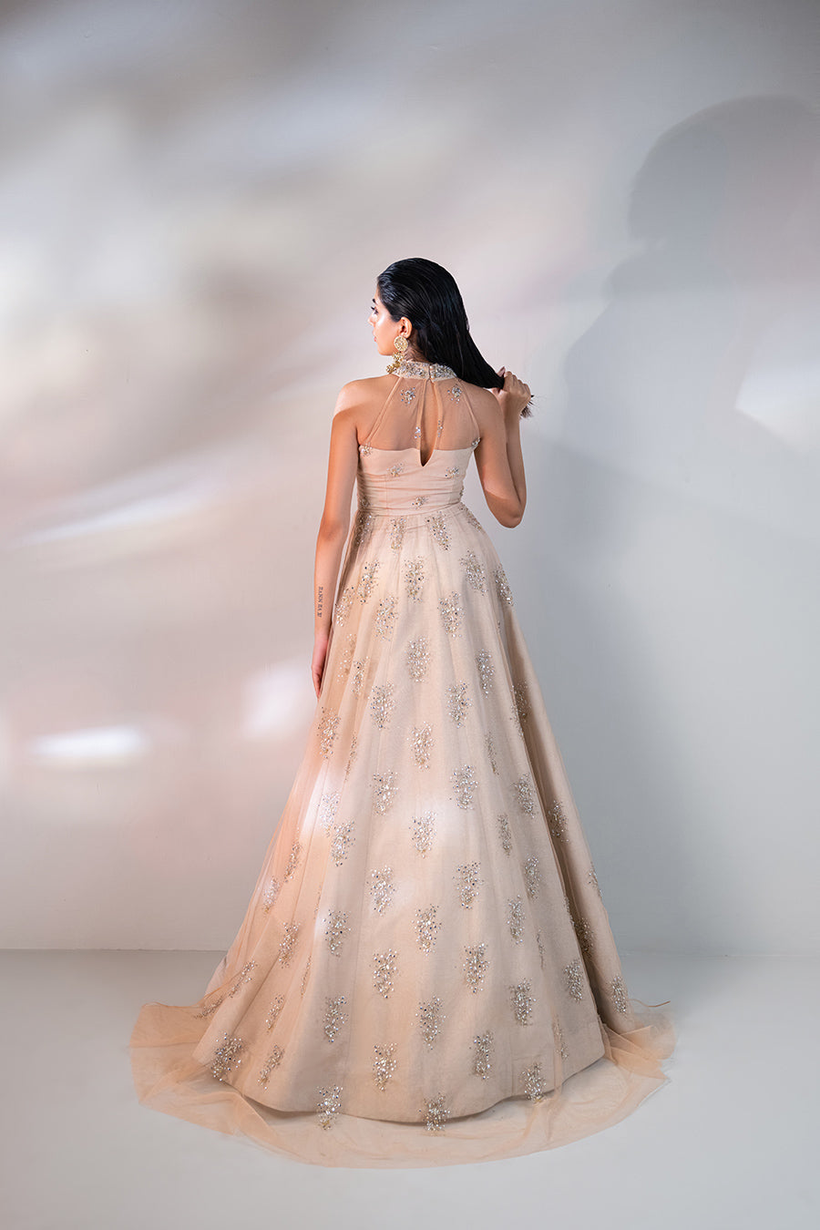 model in a back shot wearing a formal net mandarian collar with a front open slit shirt and paired with a shimmer light peach lehnga and a mokaish dupatta