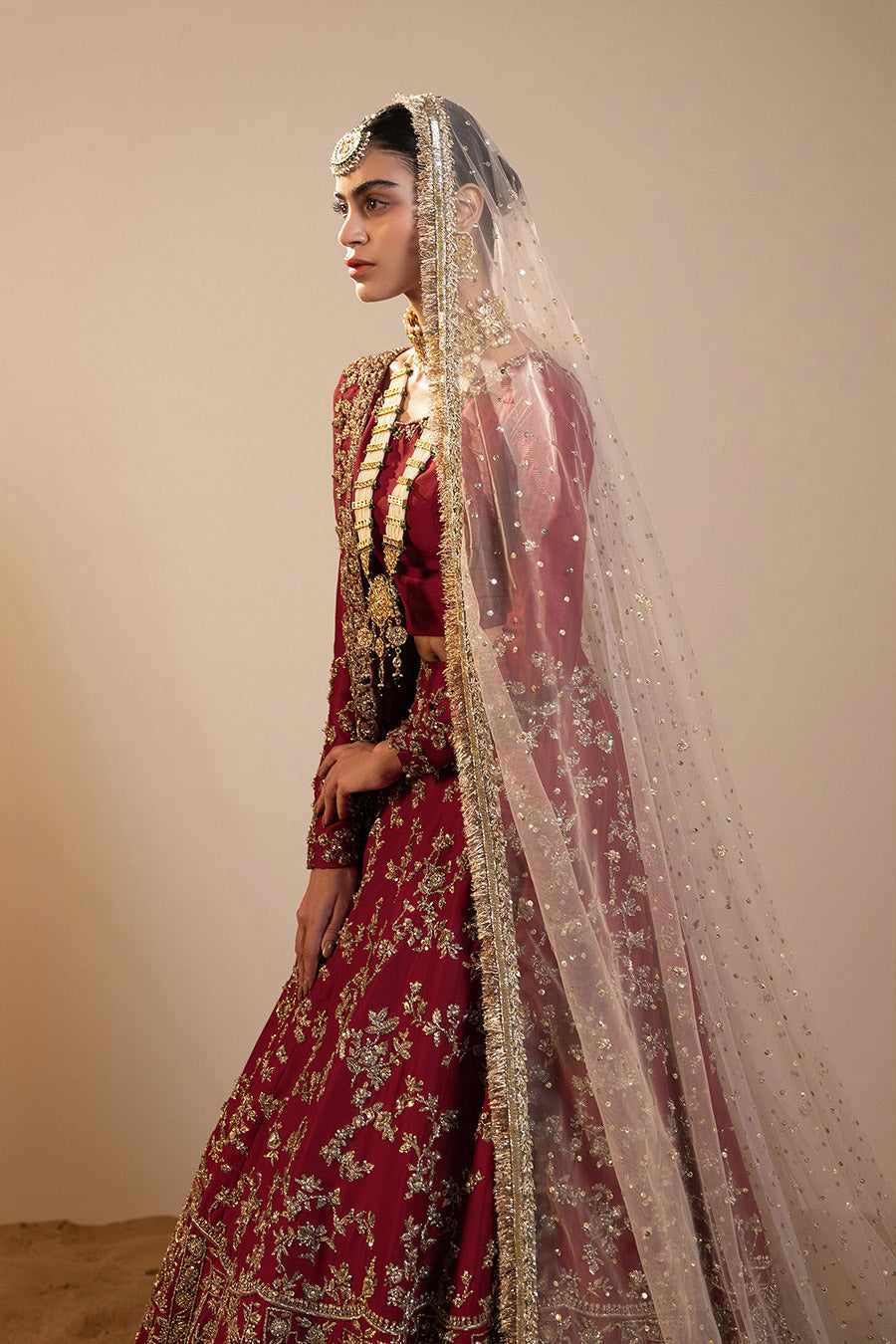 Model in a closeup side shot wearing maroon raw silk lehenga choli paired with silk dupatta and net veil