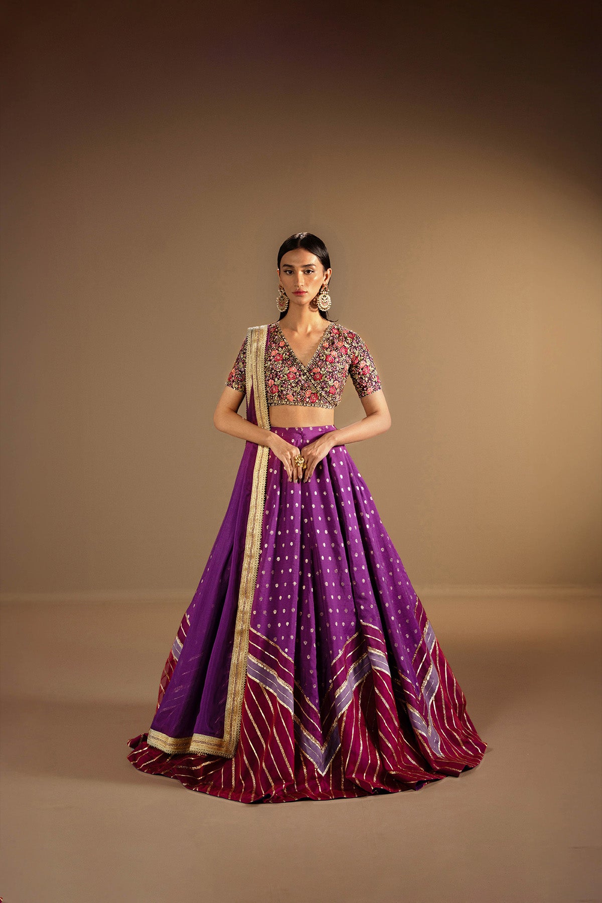 A woman wearing a traditional outfit consisting of a dark purple choli with sequin and thread work, a color-blocked lehenga, and a silk chiffon dupatta with lace detailing.