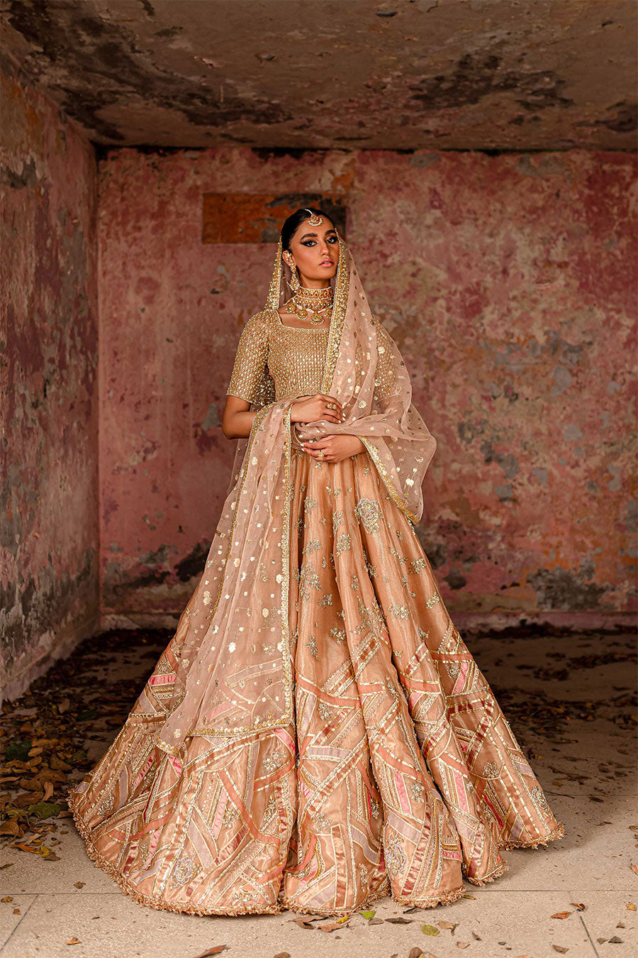 Model wearing a warm peach bridal lehenga dress with thread work, zardozi, and sequin embellishments with pastle pink dupatta by Zuria Dor