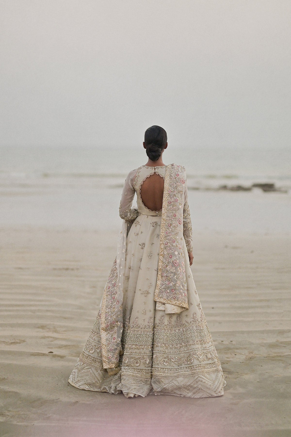 Model in a back shot wearing long pishwas gown in organza silk paired with an organza zari dupatta and organza lehenga