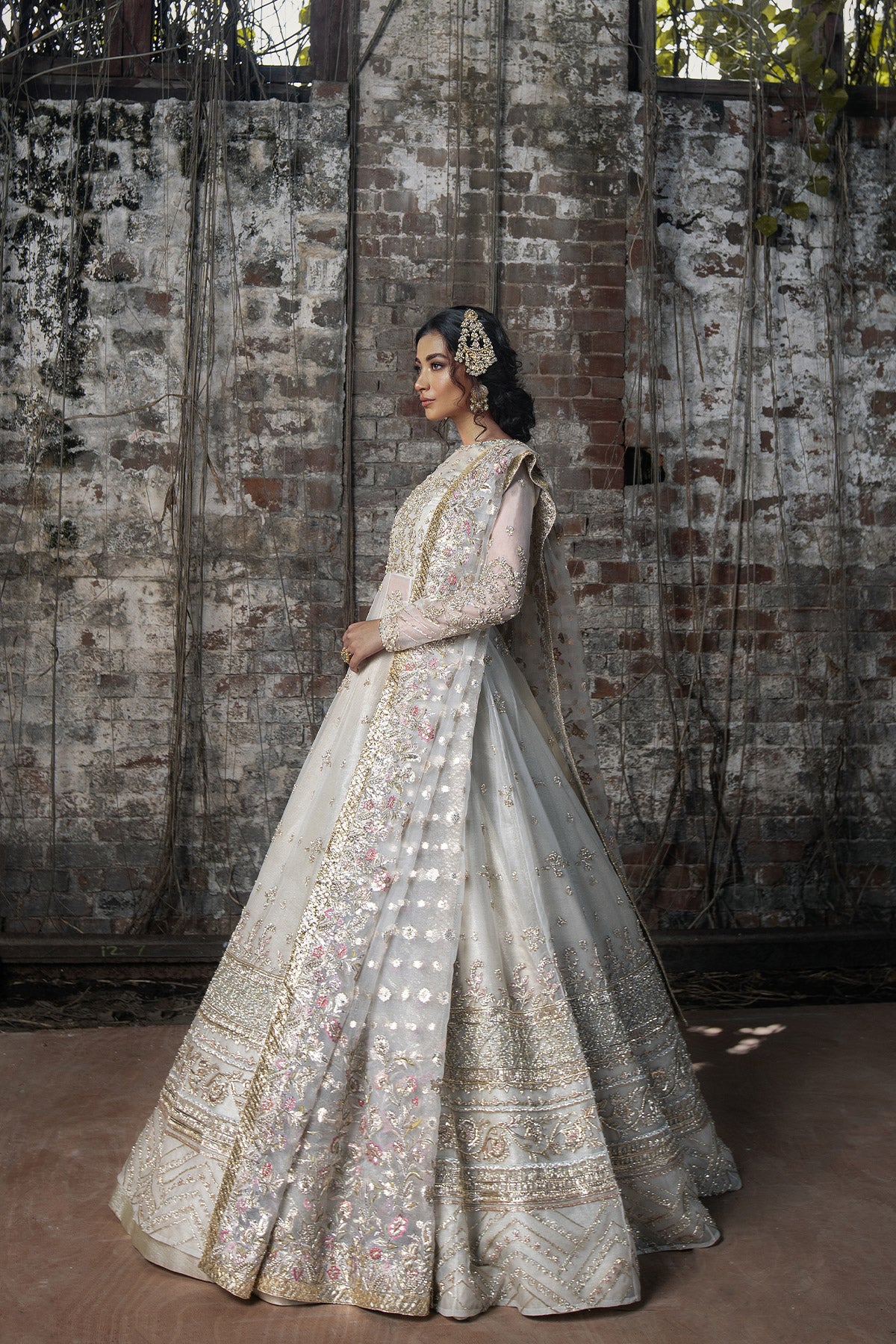 Model in a side view shot wearing long pishwas gown in organza silk paired with an organza zari dupatta and organza lehenga