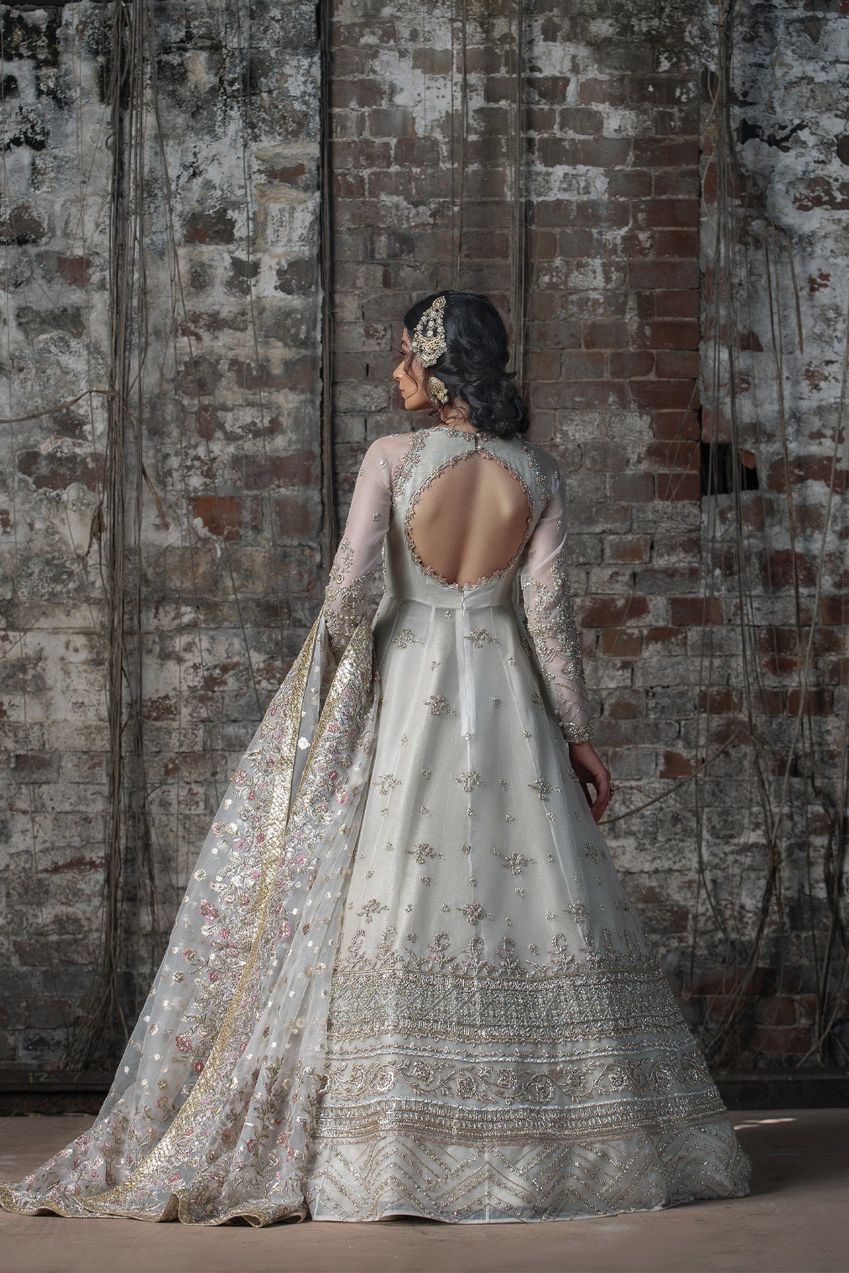 Model in a back view shot wearing long pishwas gown in organza silk paired with an organza zari dupatta and organza lehenga