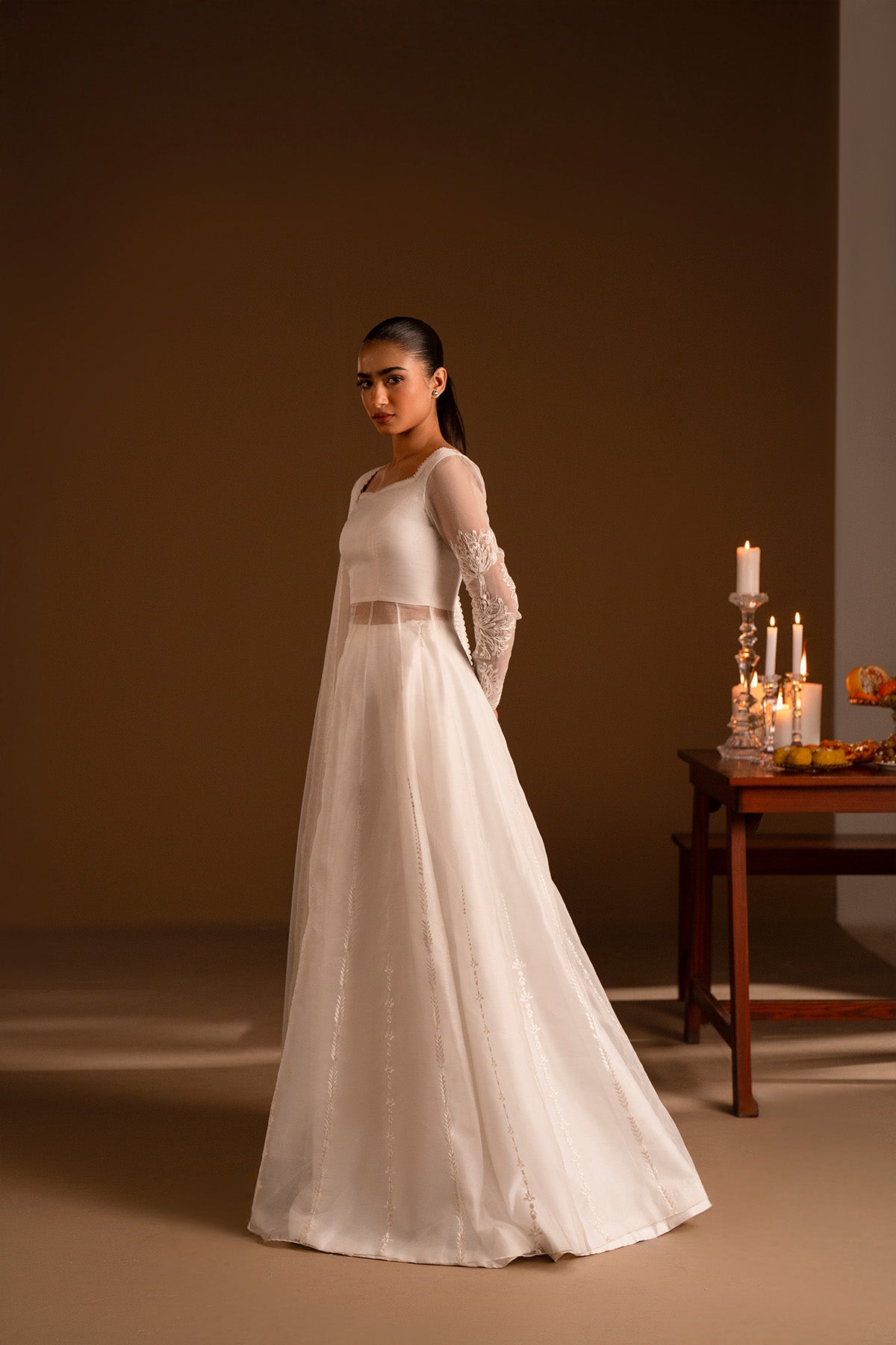 Model in a side shot wearing a long flared pishwas with embroidered shirt and organza dupatta.