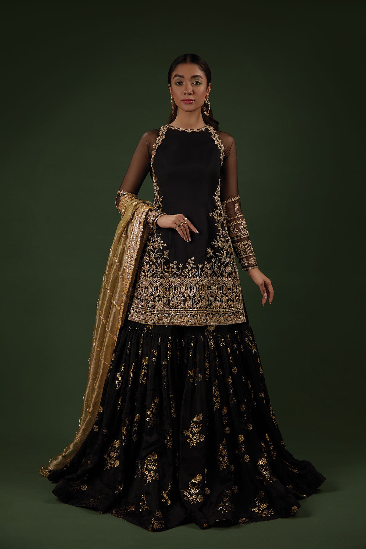 Model in a front shot wearing a black organza shirt paired with a silk chiffon foil printed gharara and an olive green tissue dupatta