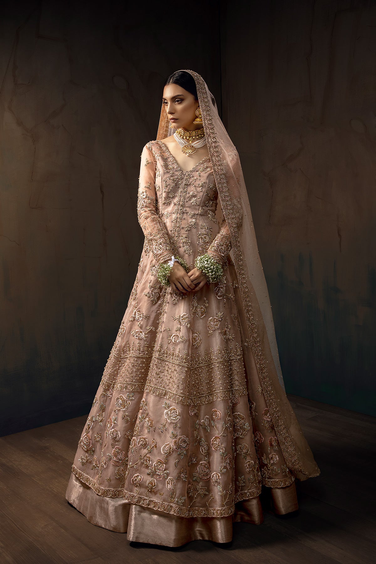 Model in a front full shot wearing blush pink bridal gown with a front slit paired with rose gold tissue lehenga and pink masuri organza dupatta