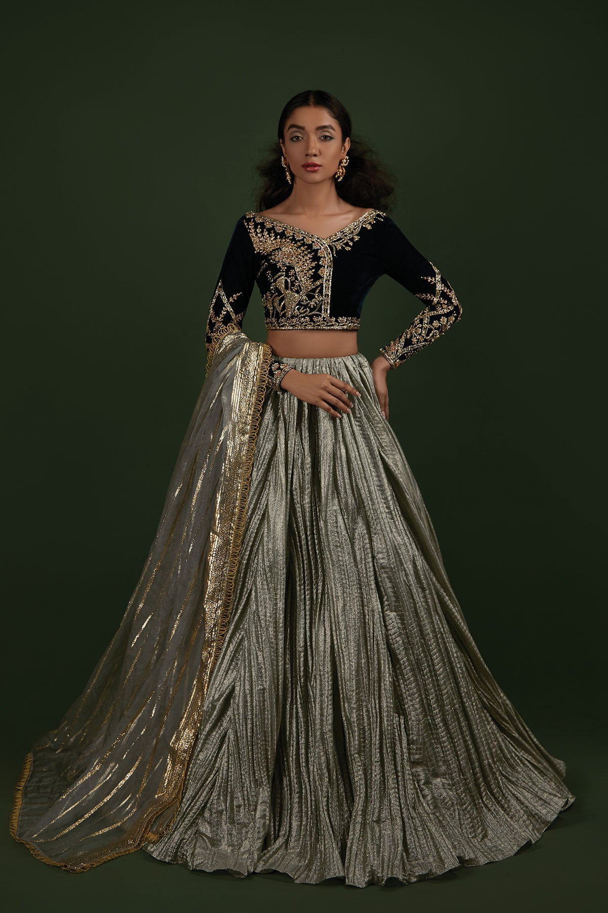 Model in a front shot wearing a formal teal velvet choli paired with a mint-ice blue crushed lehenga made of shimmered fabric and an organza zari dupatta
