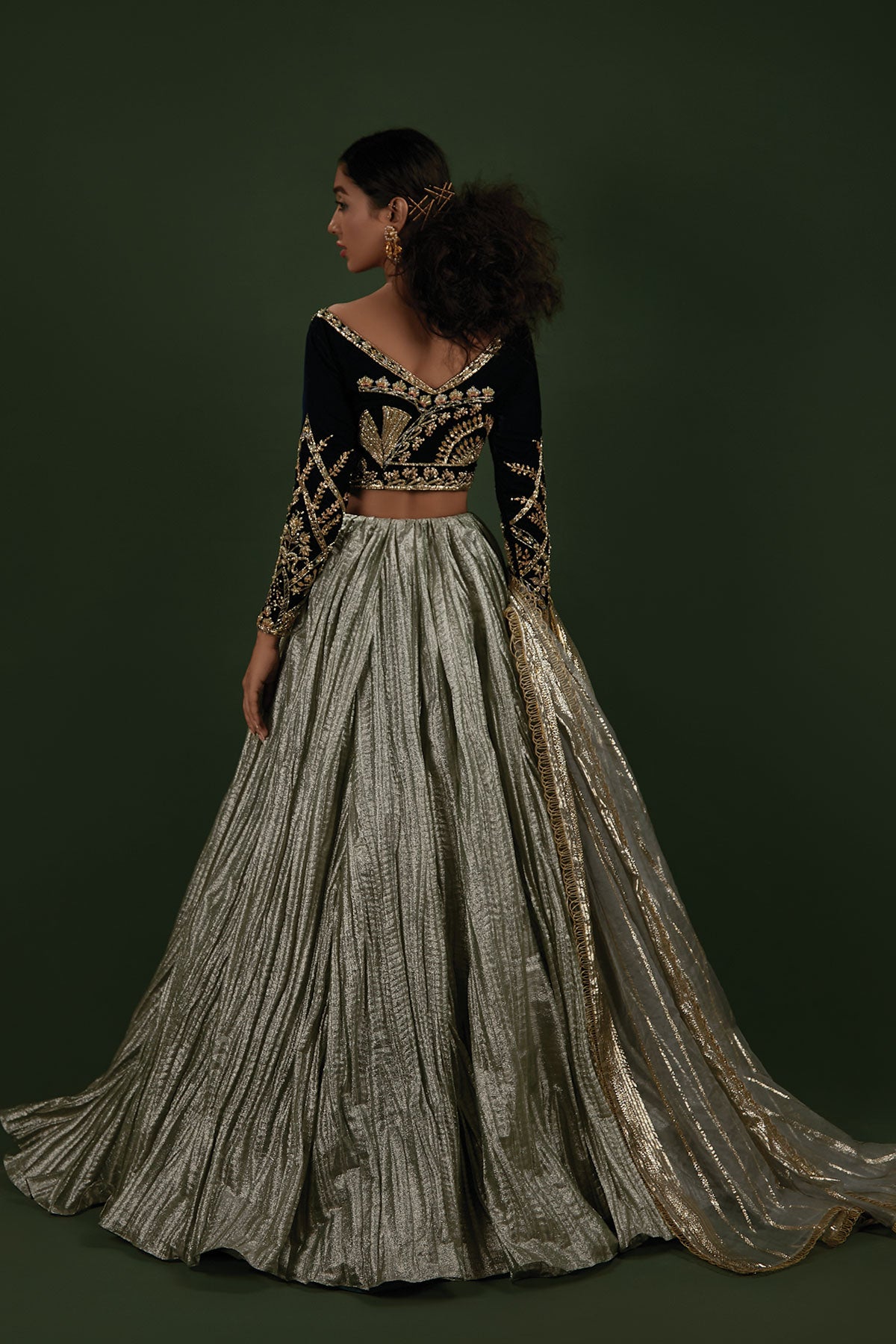 Model in a back shot wearing a formal teal velvet choli paired with a mint-ice blue crushed lehenga made of shimmered fabric and an organza zari dupatta
