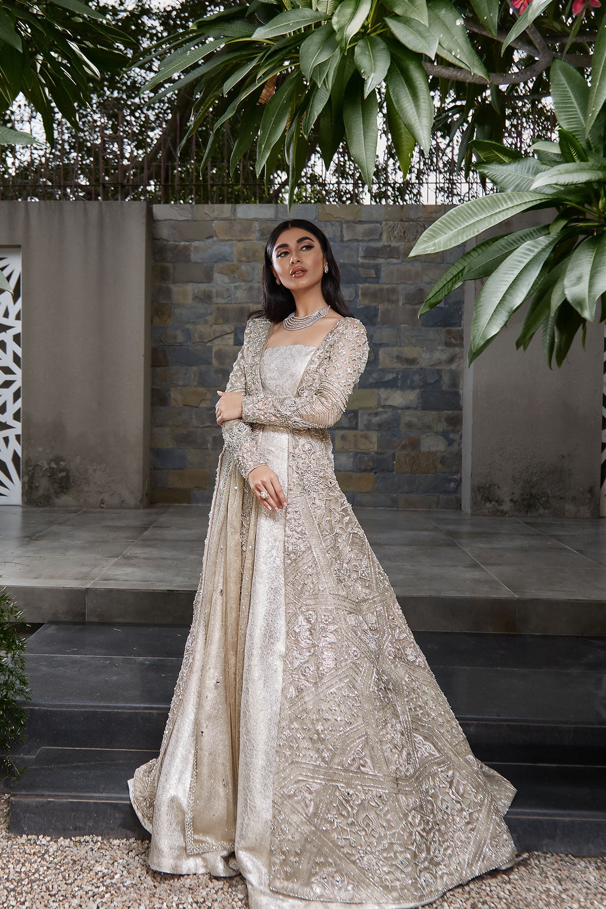 model in a side shot wearing bridal kundan net front-open long gown paired with a brocade bustier and lehenga and dupatta