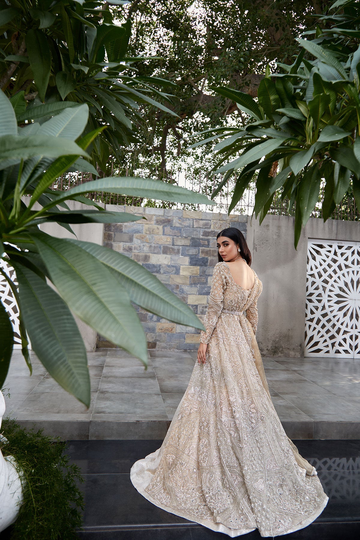 model in a back shot wearing bridal kundan net front-open long gown paired with a brocade bustier and lehenga and dupatta