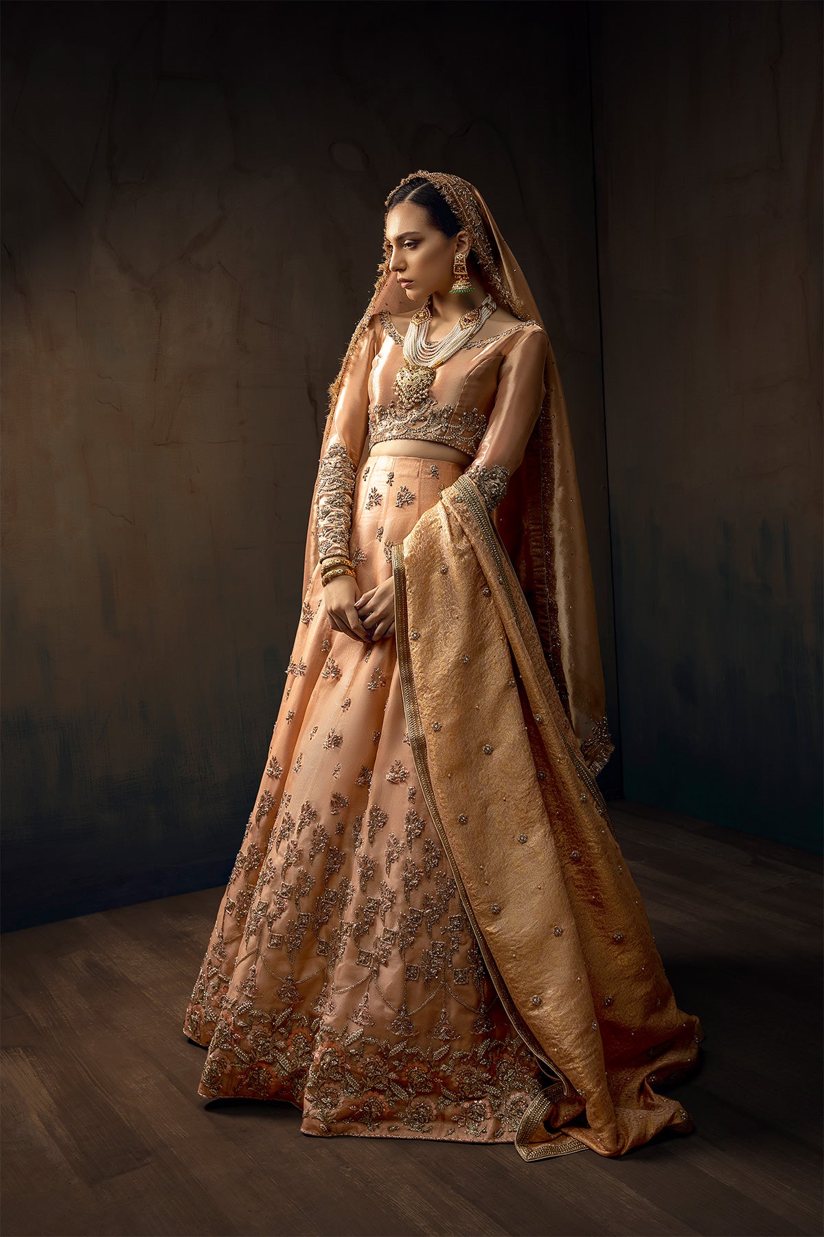 Model in a front full shot wearing melon pink lehenga in organza fabric paired with a pure tissue choli, dupatta accompanied by a jamavar shawl