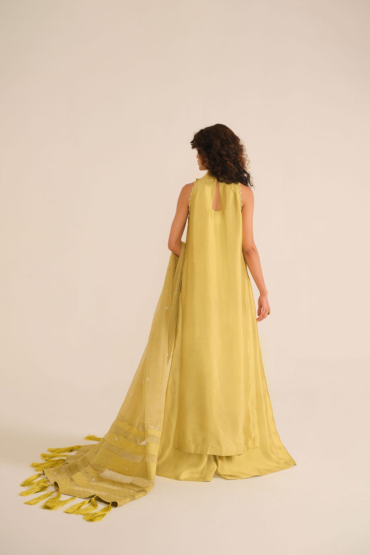 Model in a side shot wearing mustard tissue silk shirt with a halter neckline paired with flared pants and silk organza dupatta