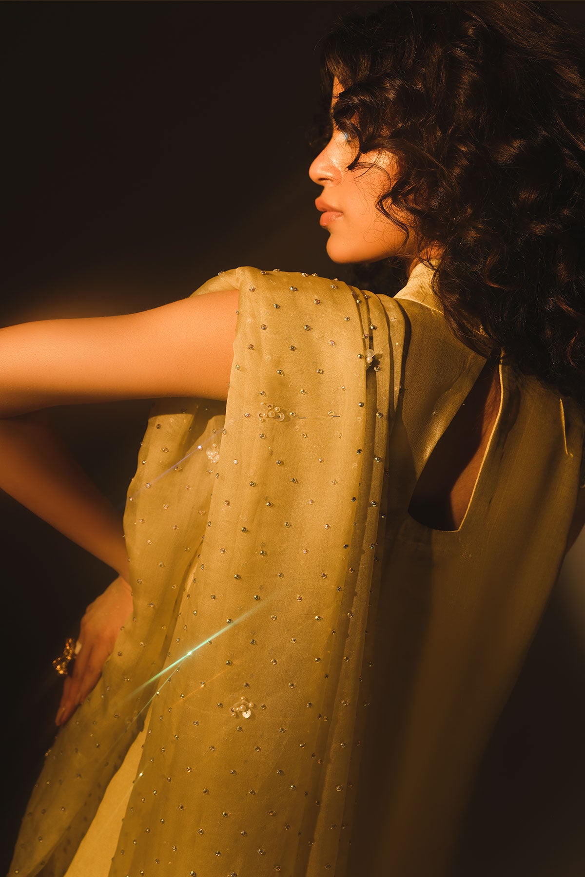 Model in a back shot wearing mustard tissue silk shirt with a halter neckline paired with flared pants and silk organza dupatta