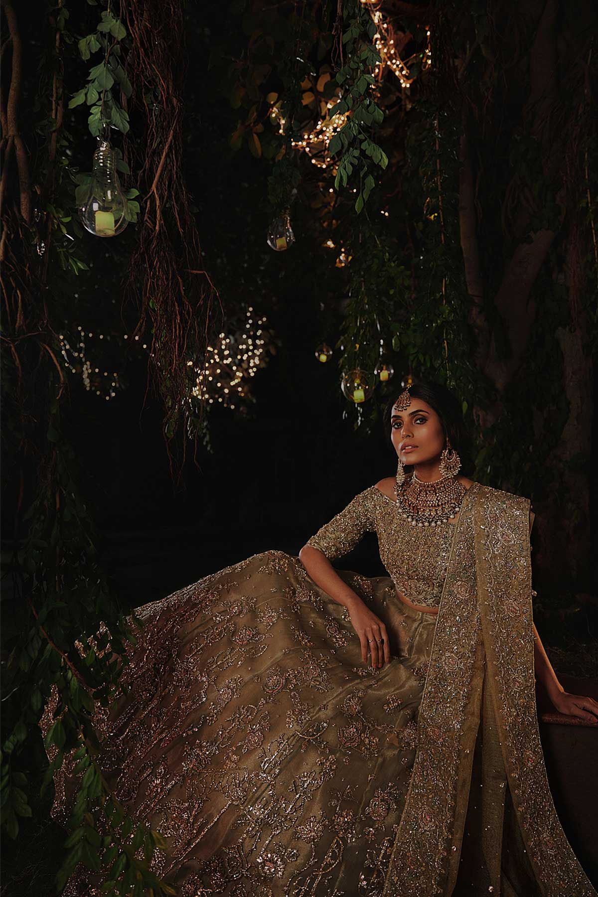model in a seated side shot wearing a bridal olive green lehenga paired with off-shoulder choli and zari net dupatta