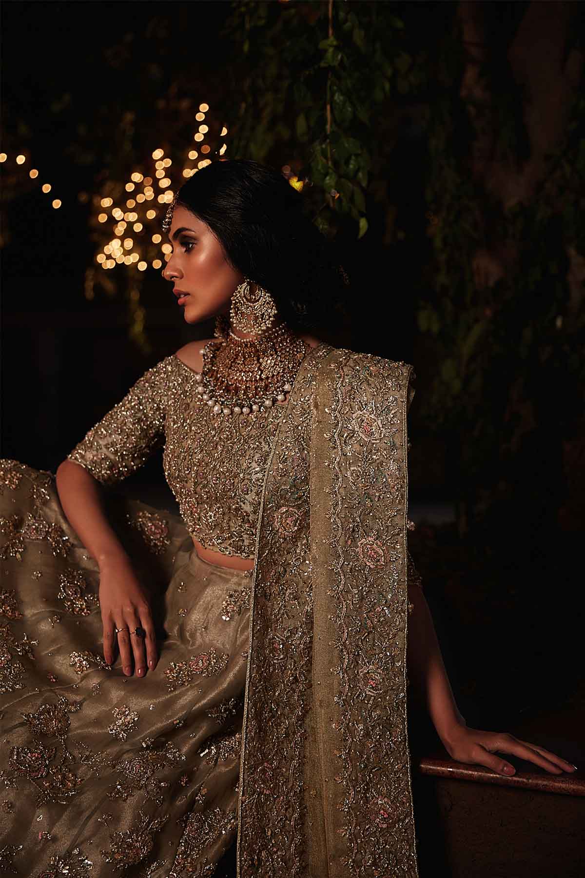 model in a closeup seated shot wearing a bridal olive green lehenga paired with off-shoulder choli and zari net dupatta
