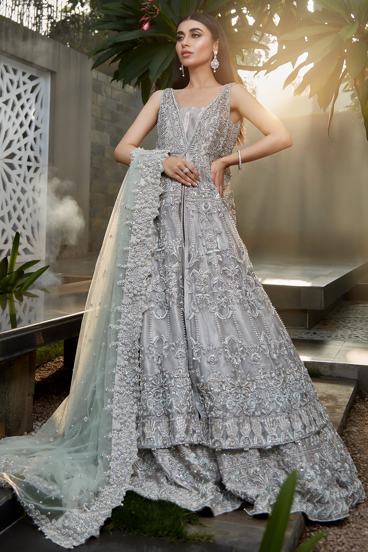 model in a front shot wearing silver bridal net front-open sleeveless gown paired with a tissue sharara and net dupatta