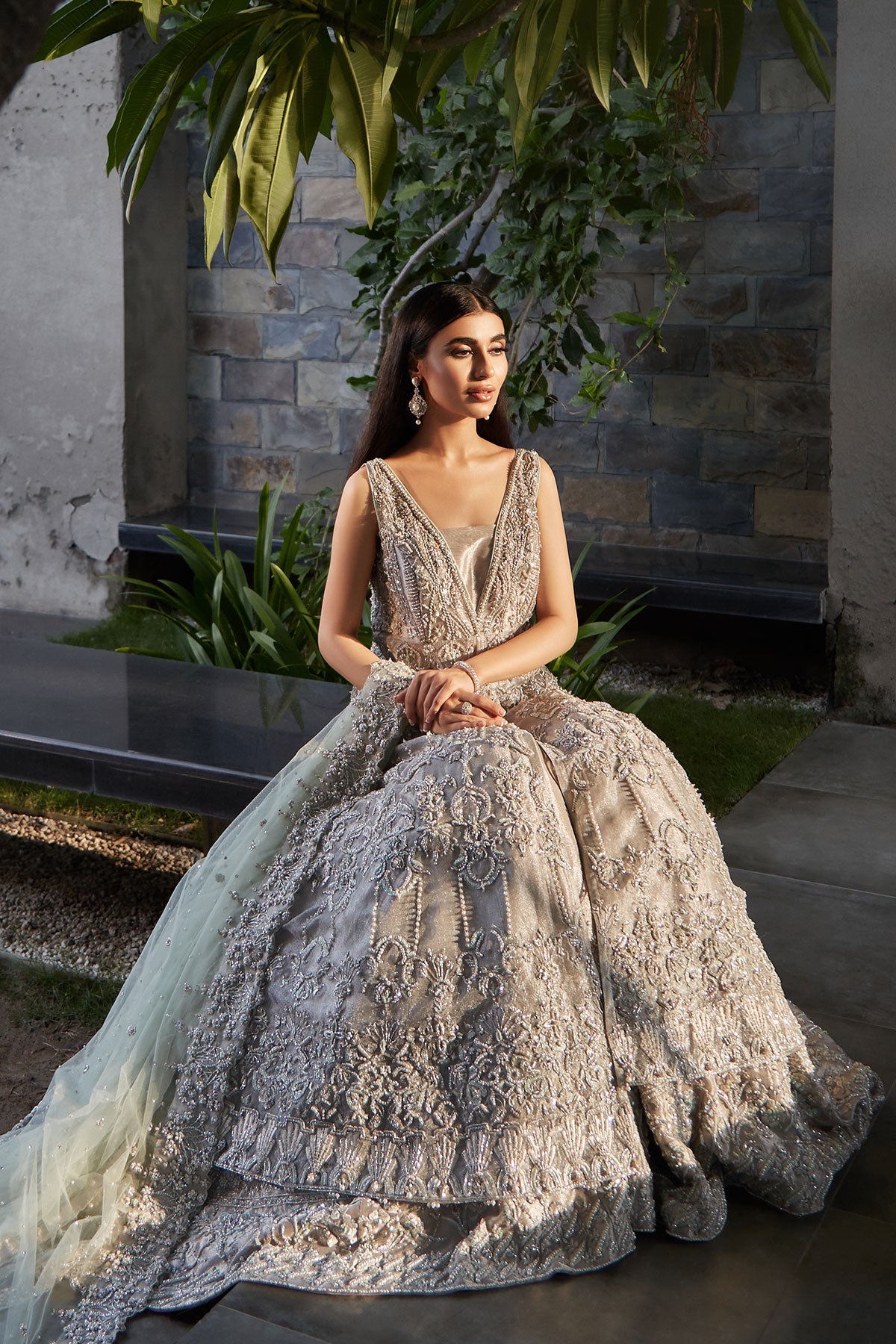 model in a seated front shot wearing silver bridal net front-open sleeveless gown paired with a tissue sharara and net dupatta