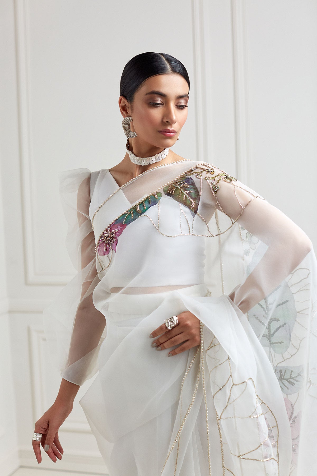 model in a front shot wearing hand-painted white organza floral saree paired with a draped one-sleeved organza blouse