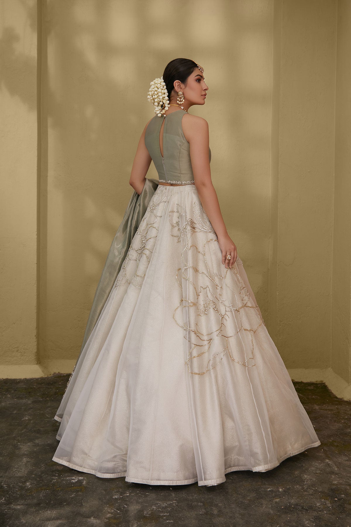 Model in a back shot wearing white organza skirt paired with green tissue blouse and an embroidered tissue dupatta