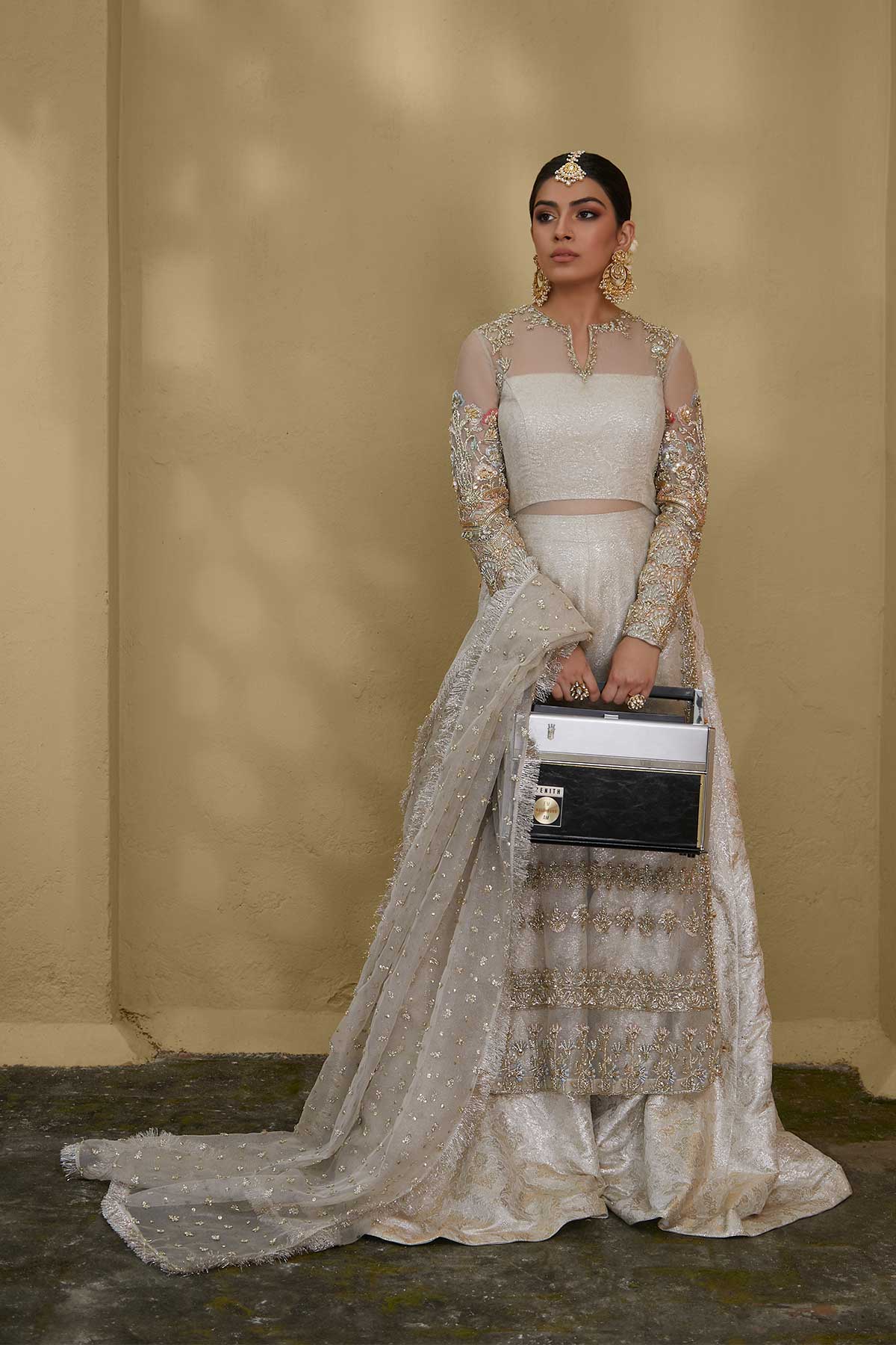 Model in a front shot wearing white kundan net shirt paired with silk brocade sharara pants and a bustier and a kundan net dupatta