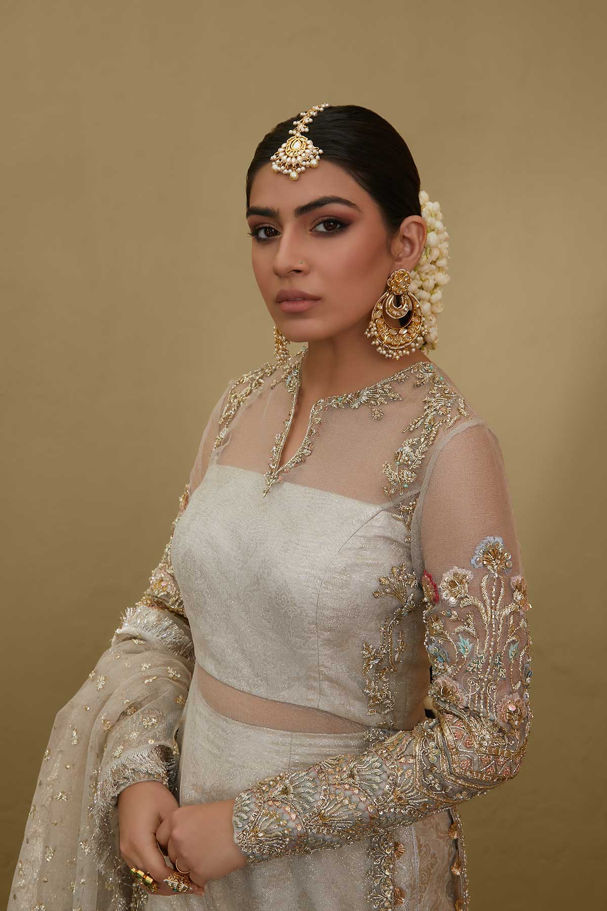 Model in a closeup shot wearing white kundan net shirt paired with silk brocade sharara pants and a bustier and a kundan net dupatta