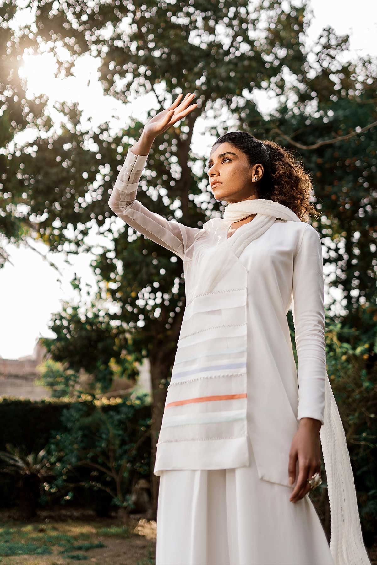 Model in a low angle shot wearing jacket with a sheer organza side paired paired with flared pants, a bustier, and a crushed dupatta