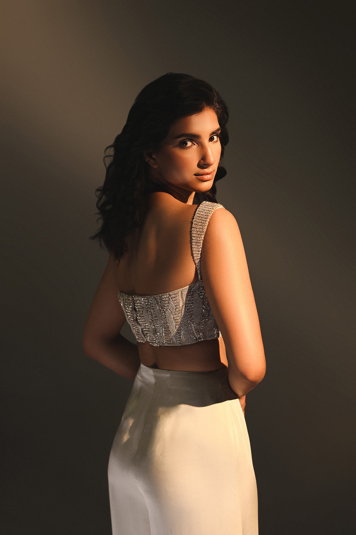 Woman wearing a patterned top and white pants against a dark background