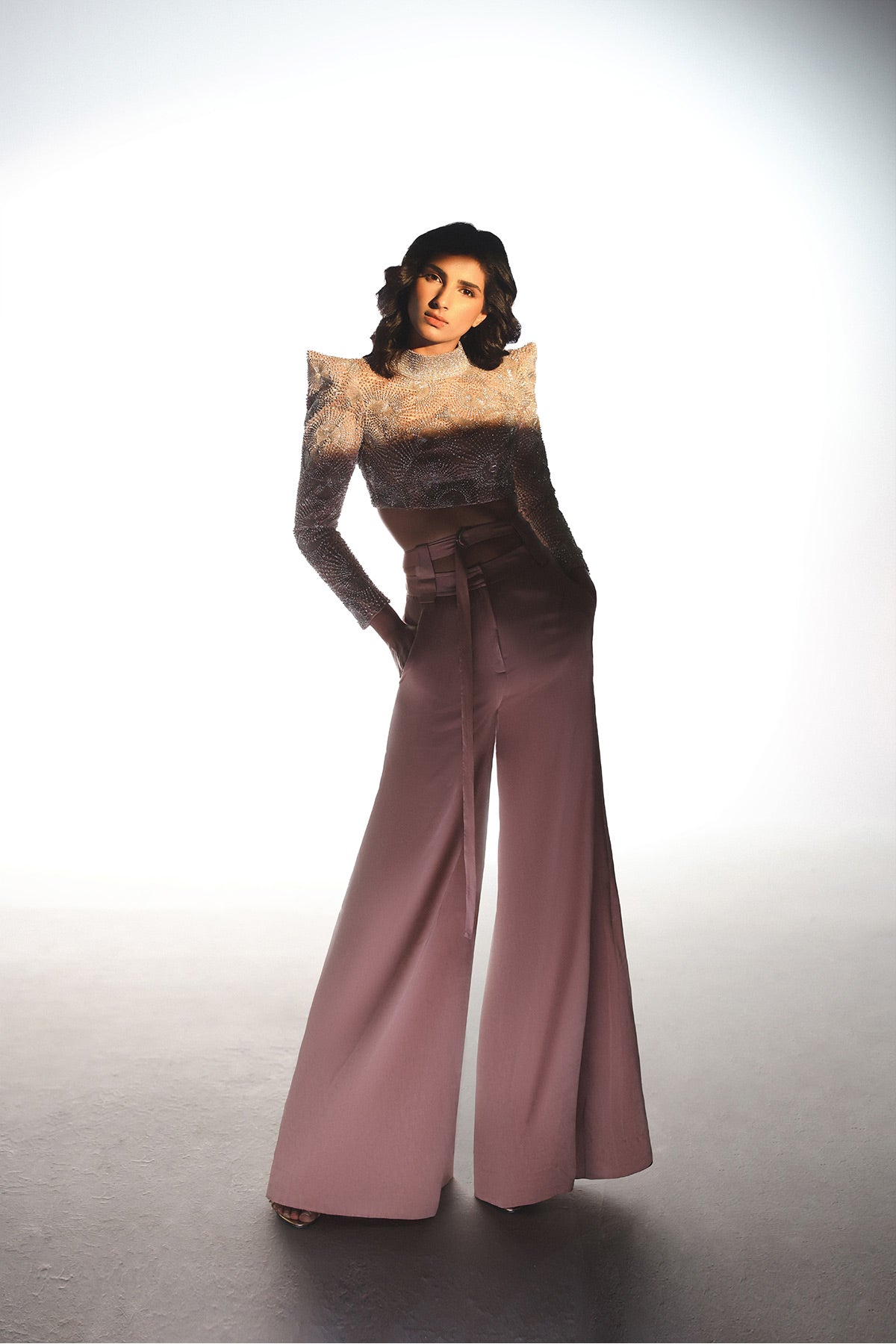 Person wearing a vintage outfit with a high-waisted dress and wide-leg pants on a plain background