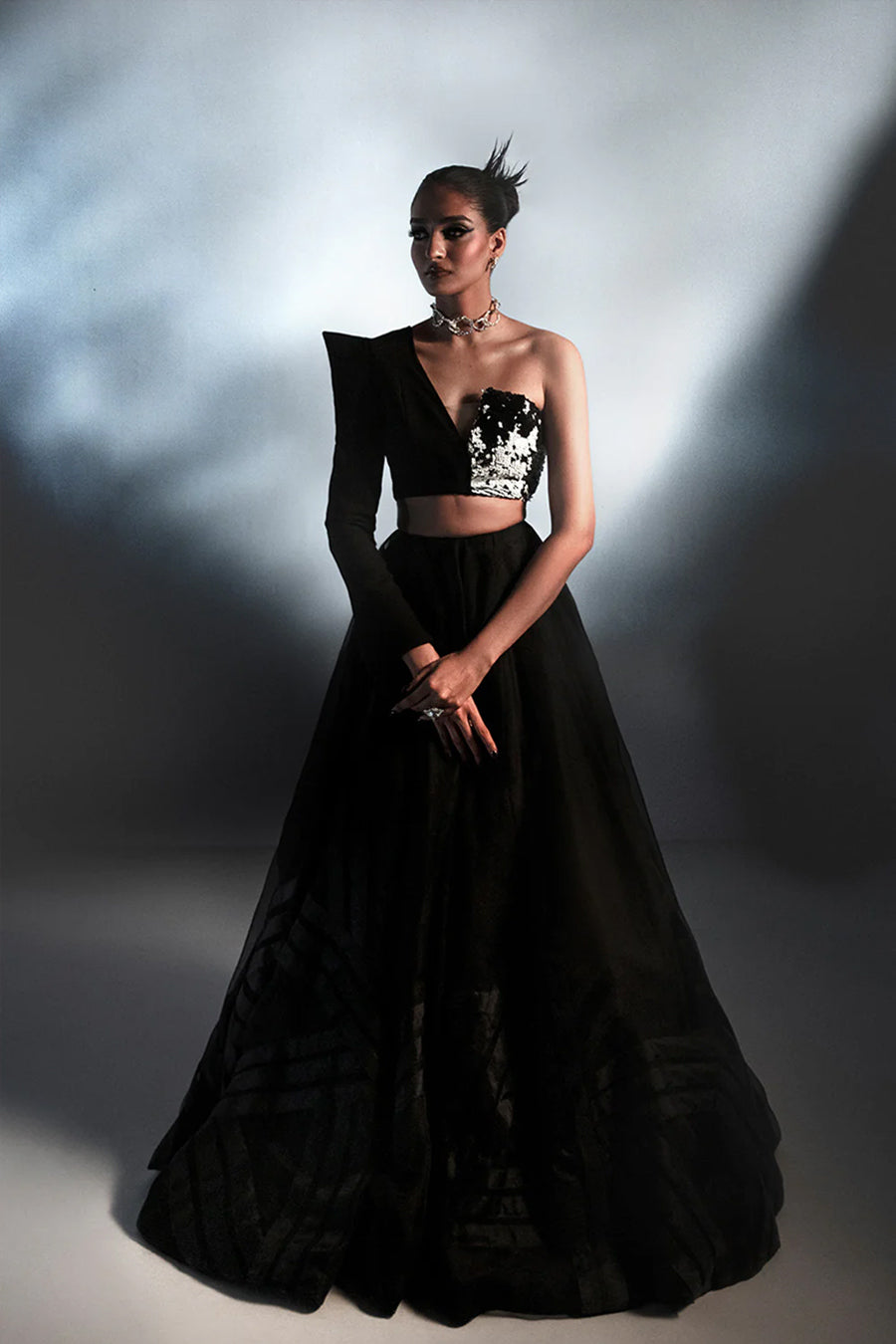 Model in a front shot wearing a black formal silk organza flared skirt paired with a one-sleeved asymmetric blouse with a pagoda shoulder