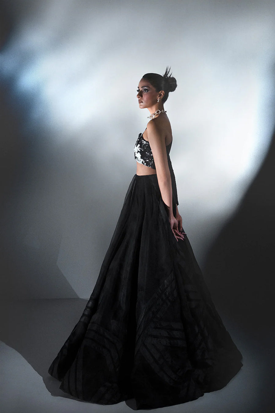 Model in a side shot wearing a black formal silk organza flared skirt paired with a one-sleeved asymmetric blouse with a pagoda shoulder