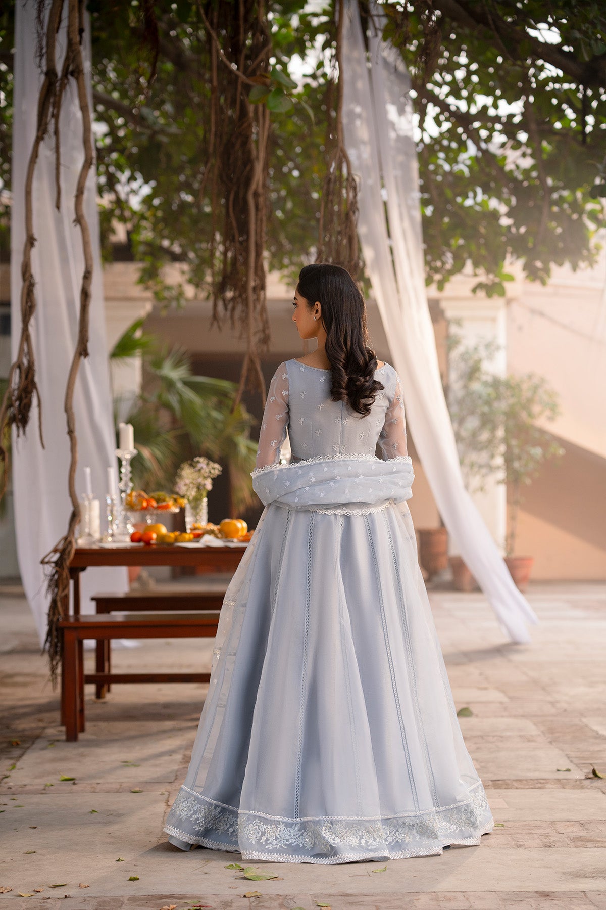 Model in a back shot wearing embroidered pishwas with organza dupatta & raw silk pants