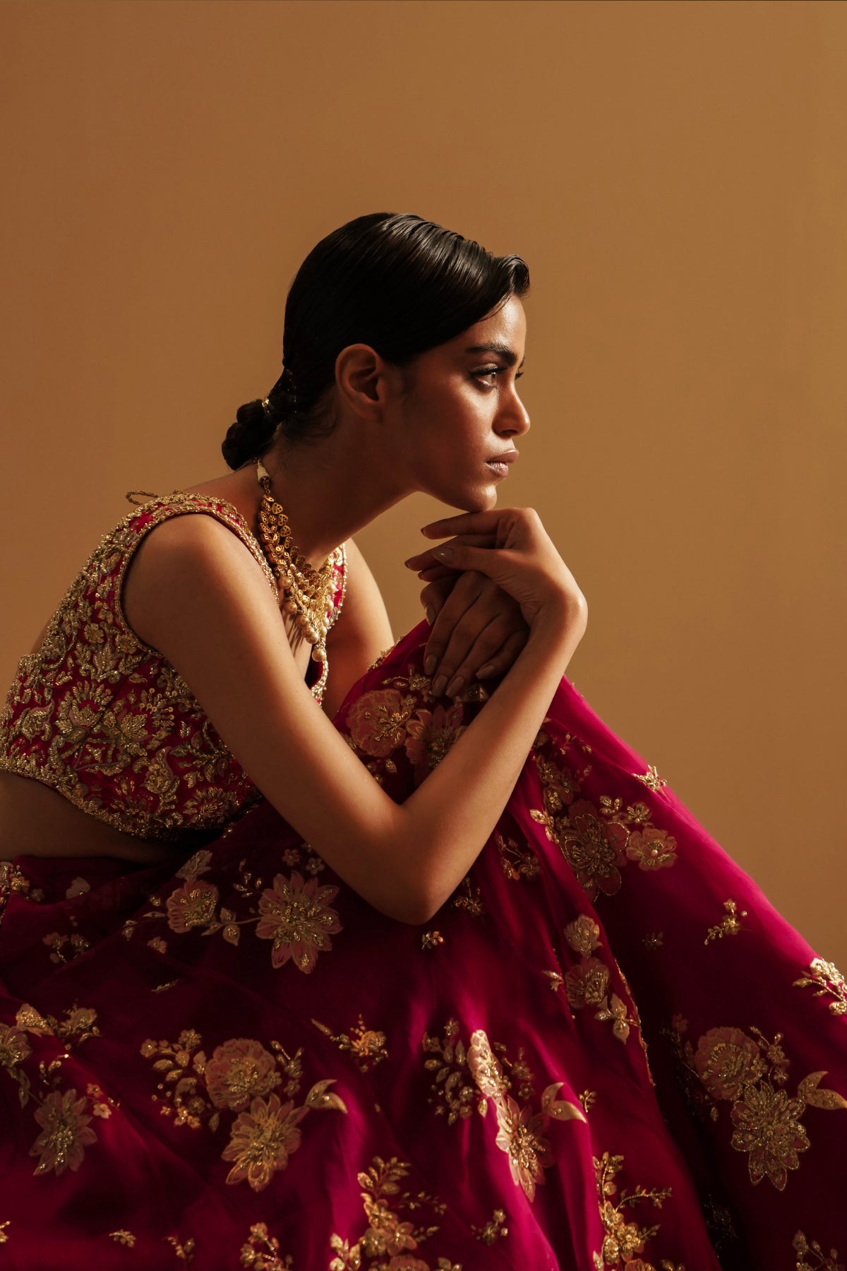 Model in a seated side view angle wearing a dark pink lehenga choli with handcrafted zardozi and sequin work