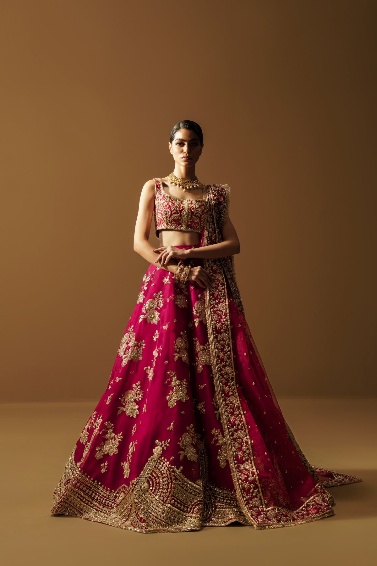 Model in a back view angle wearing a dark pink lehenga choli with handcrafted zardozi and sequin work and an organza dupatta