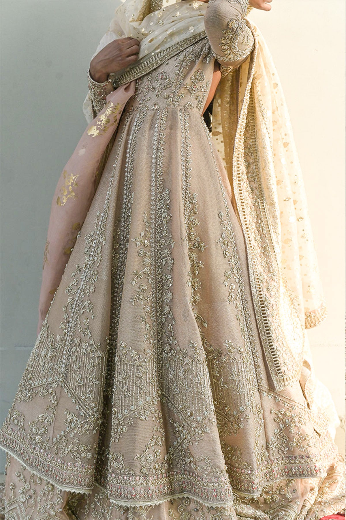 Model in a closeup shot wearing a dusty pink pishwas paired with lehenga along with an organza zari dupatta with colored and embellished borders 