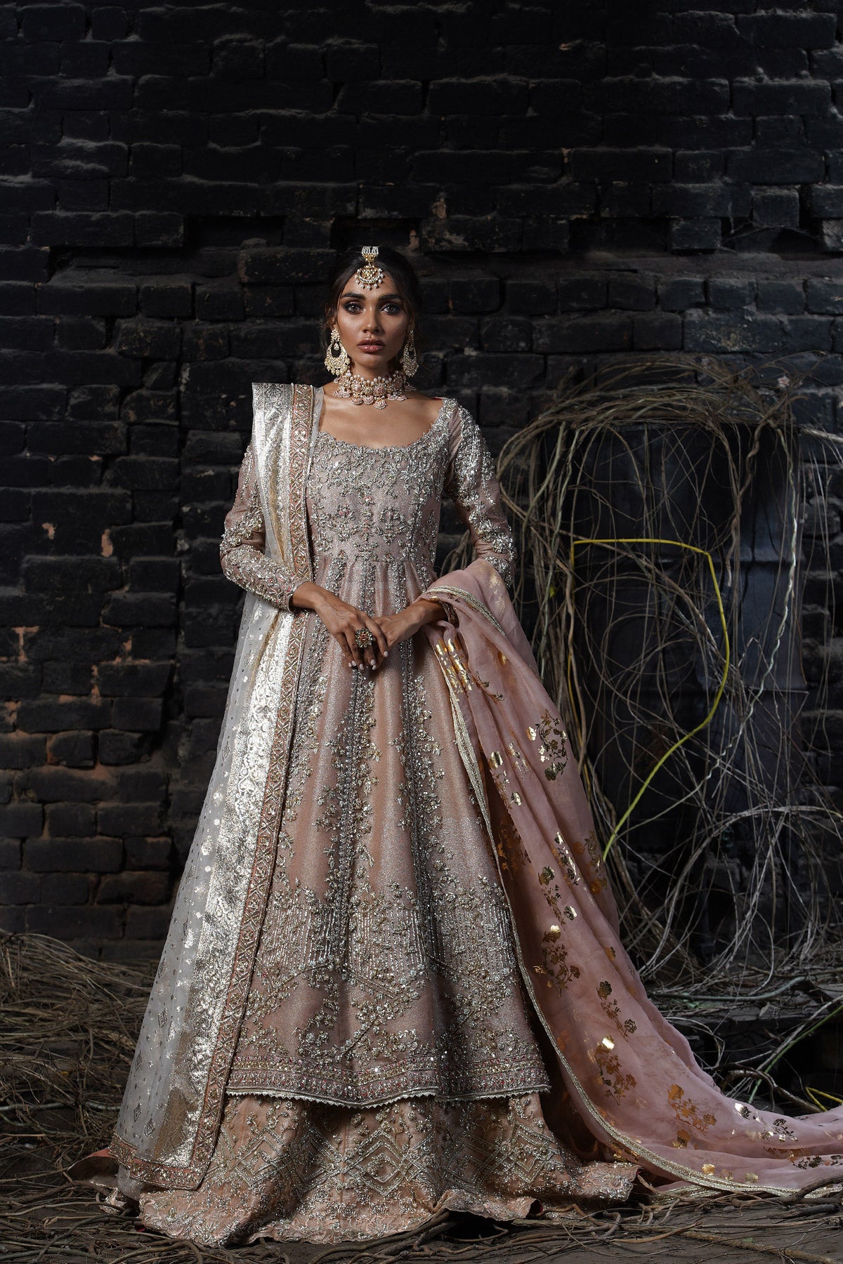 Model in a front shot wearing a dusty pink pishwas paired with lehenga  along with an organza zari dupatta with colored and embellished borders 