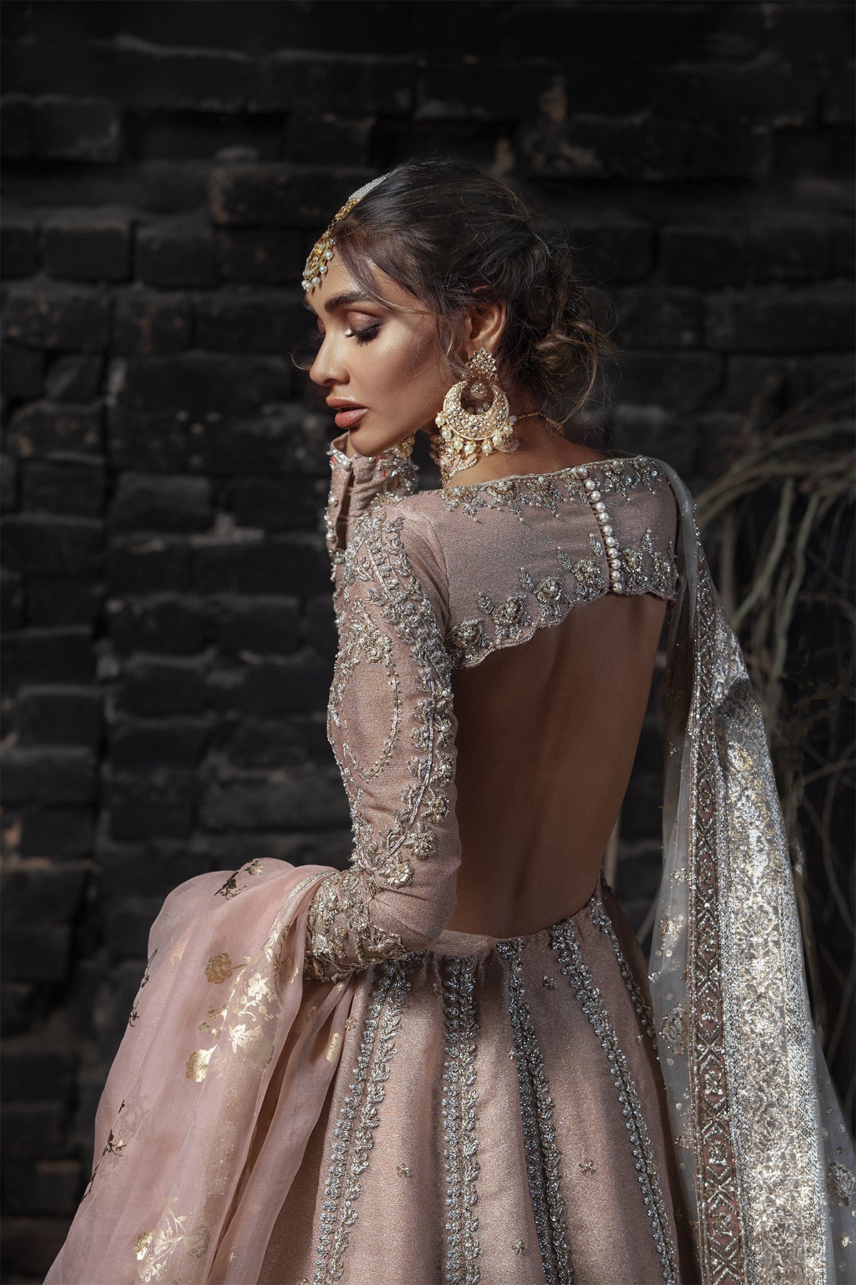 Model in a closeup back shot wearing a dusty pink pishwas along with an organza zari dupatta with colored and embellished borders 