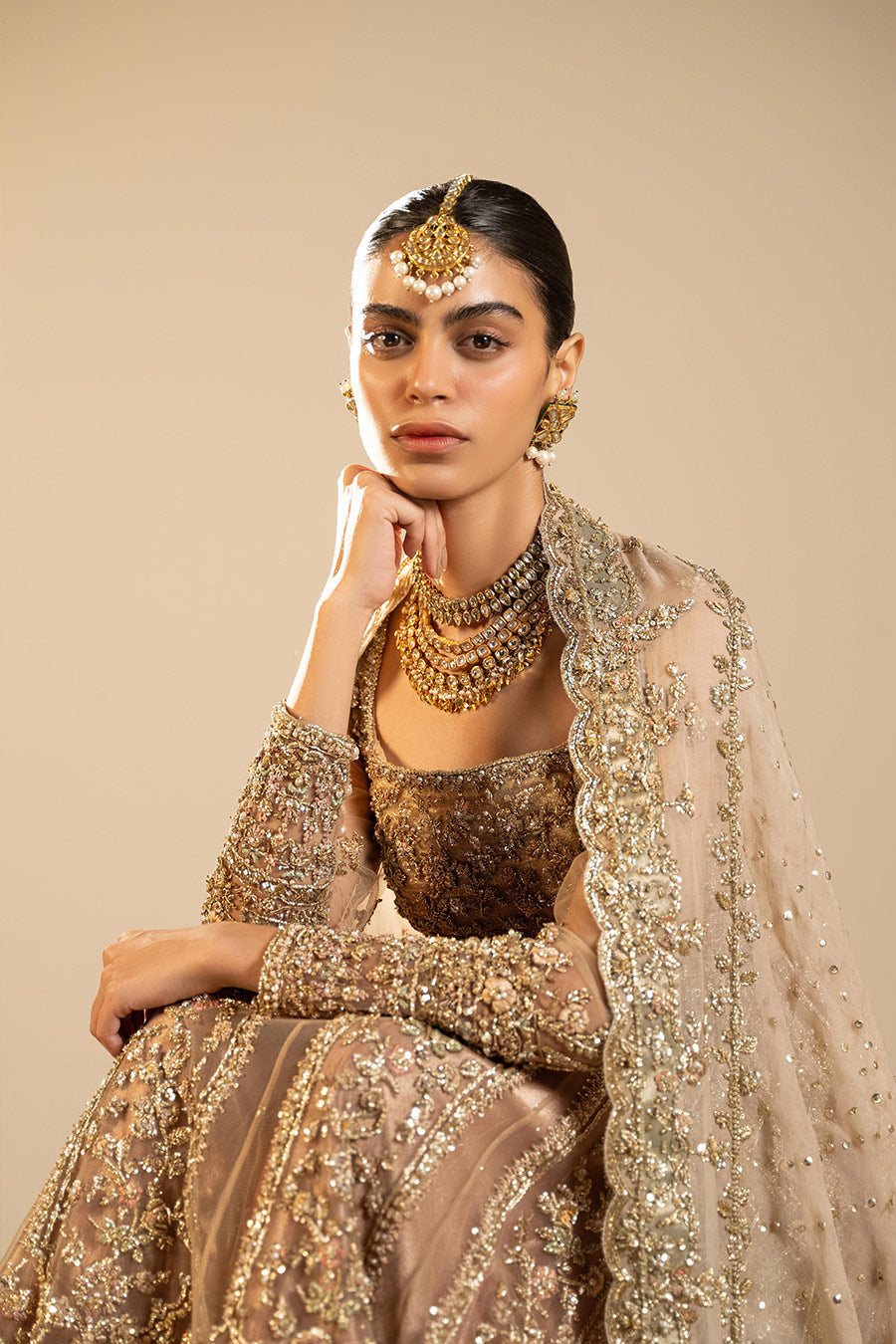 Model in a closeup seated shot wearing dusty pink net pishwas combined with a farshi sharara and a dusty pink silk organza dupatta 